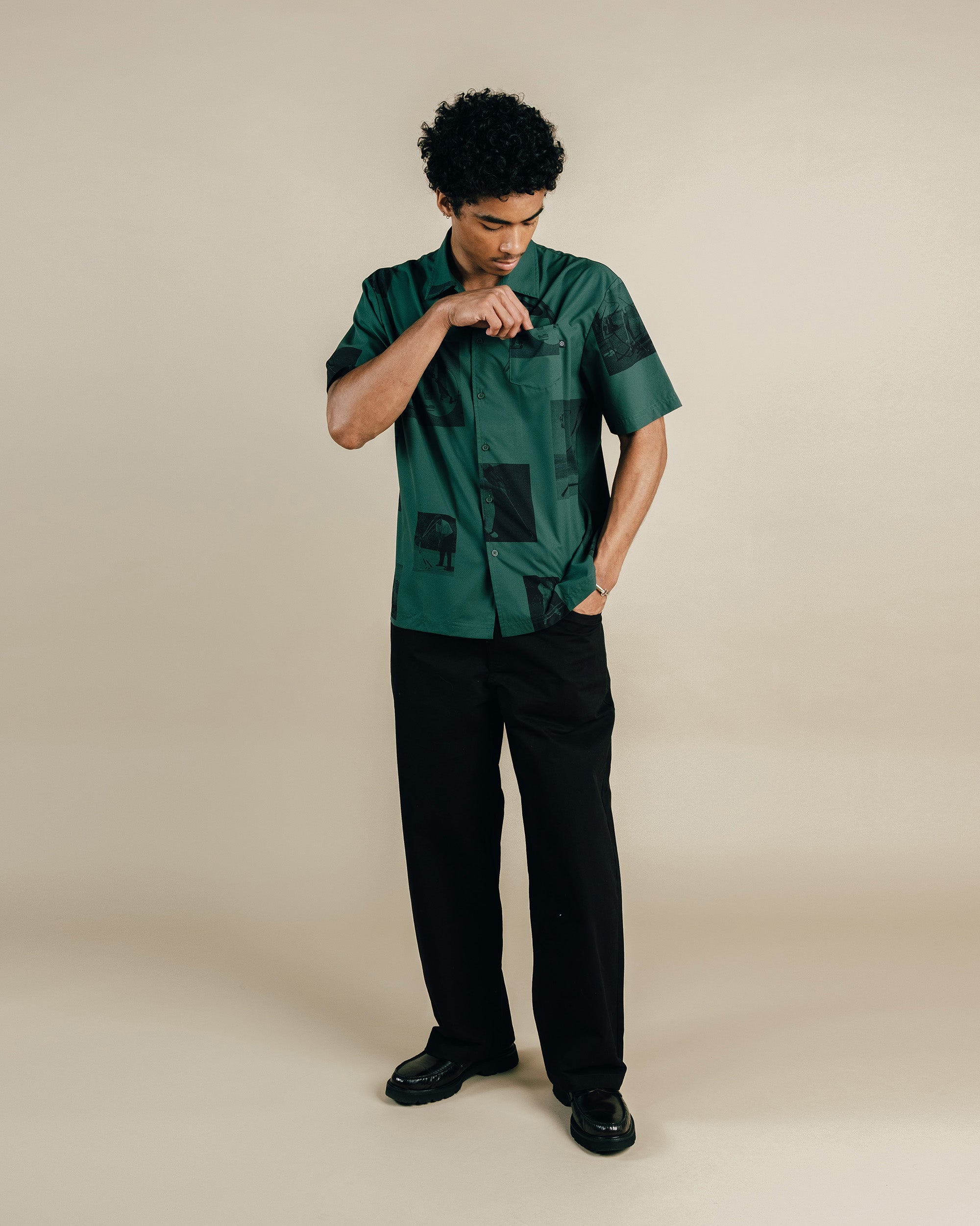 Man wearing a green patterned shirt and black pants on a beige background