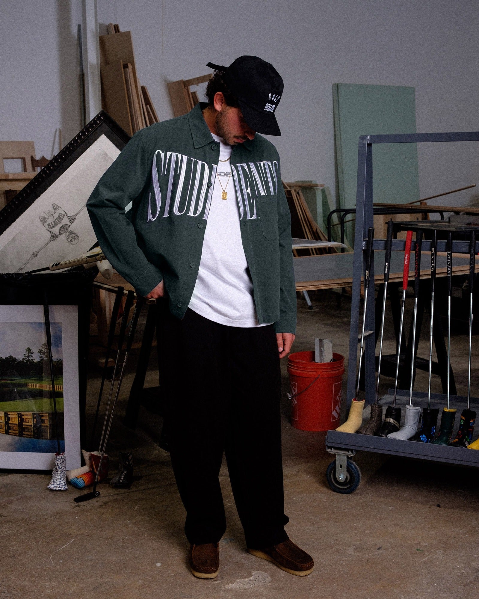 Person wearing a green jacket with 'STUDIENREISE' text in an indoor setting with tools and materials.