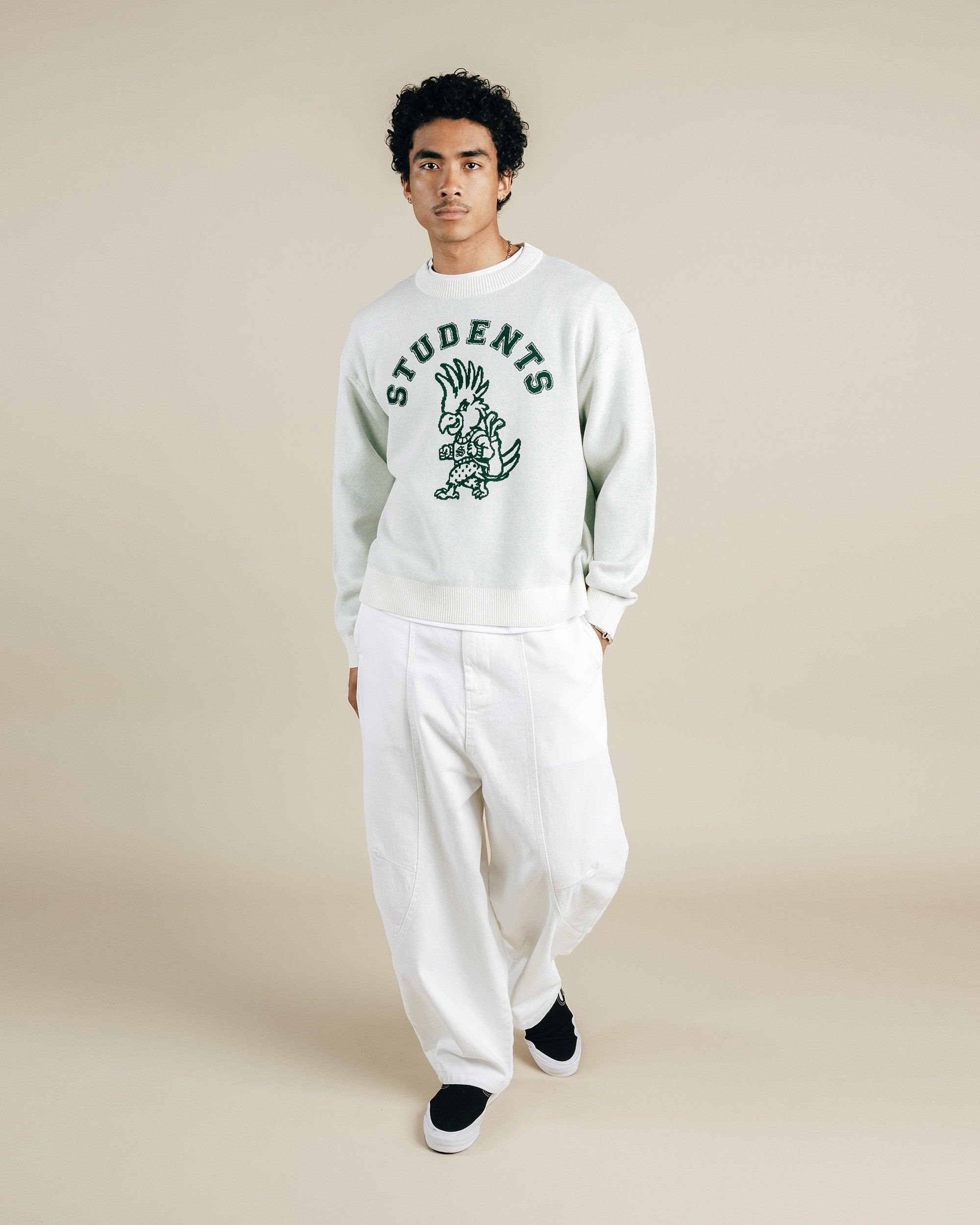 Person wearing a white sweatshirt with a graphic design and text, standing against a beige background