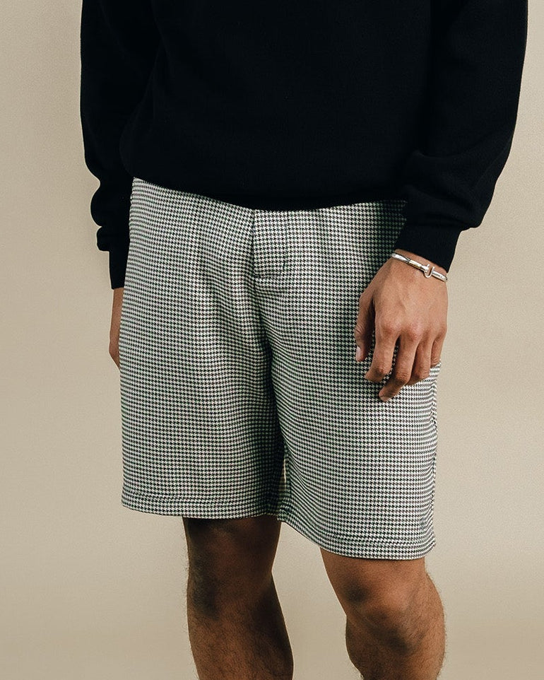 Person wearing a black sweatshirt with 'STUDENTS' text and gray shorts on a beige background