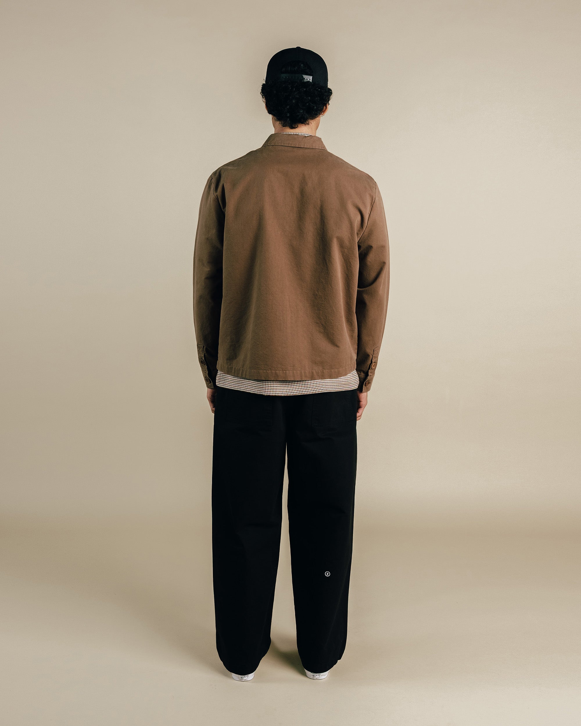 Person wearing a brown jacket and black pants on a beige background