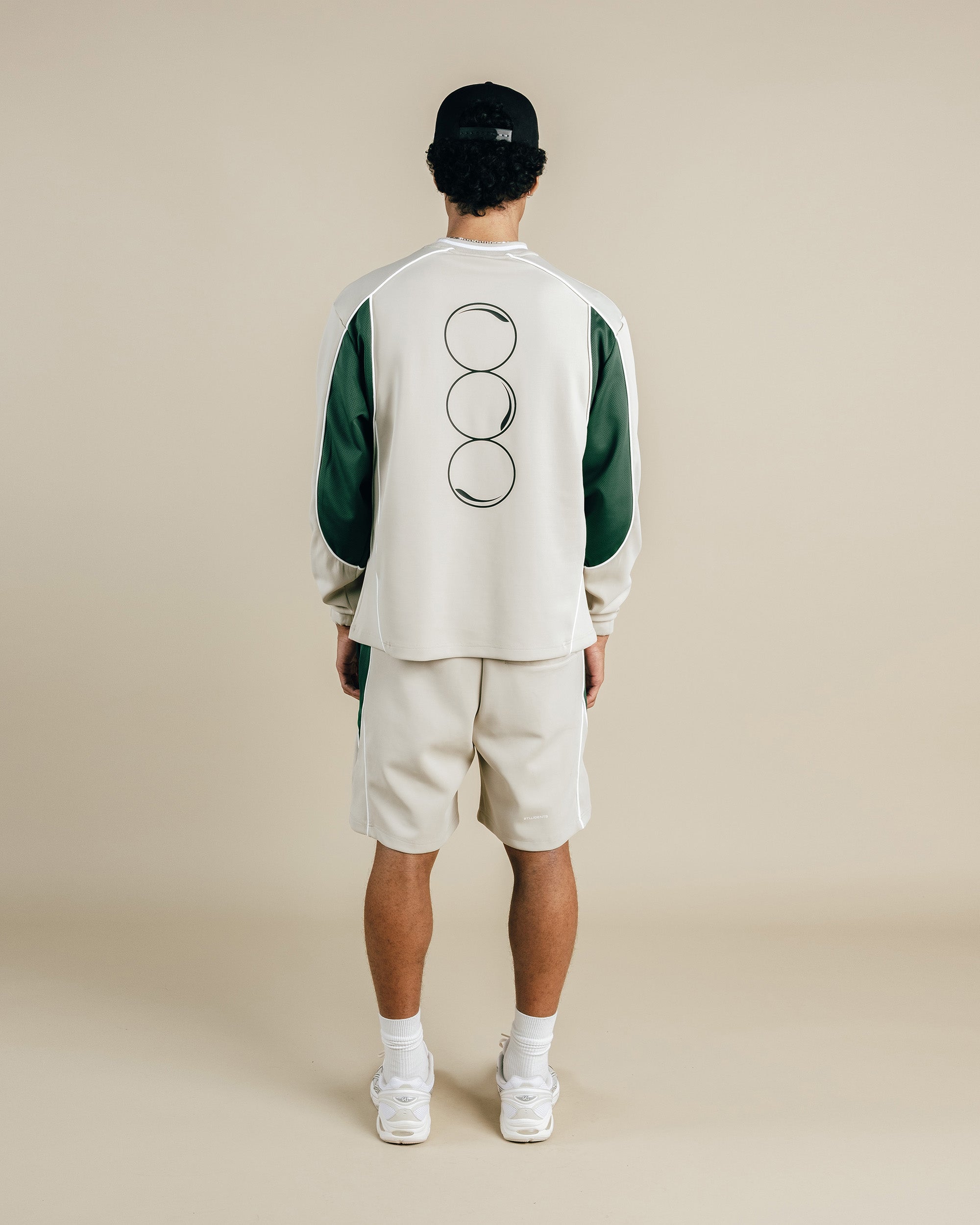 Person wearing a green and beige outfit with a logo on the back against a beige background