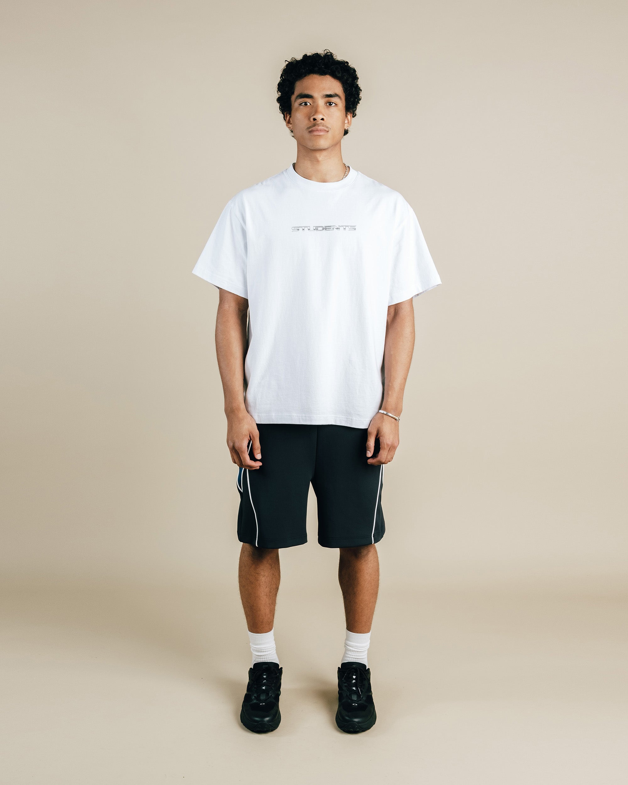 Person wearing a white t-shirt and black shorts on a beige background