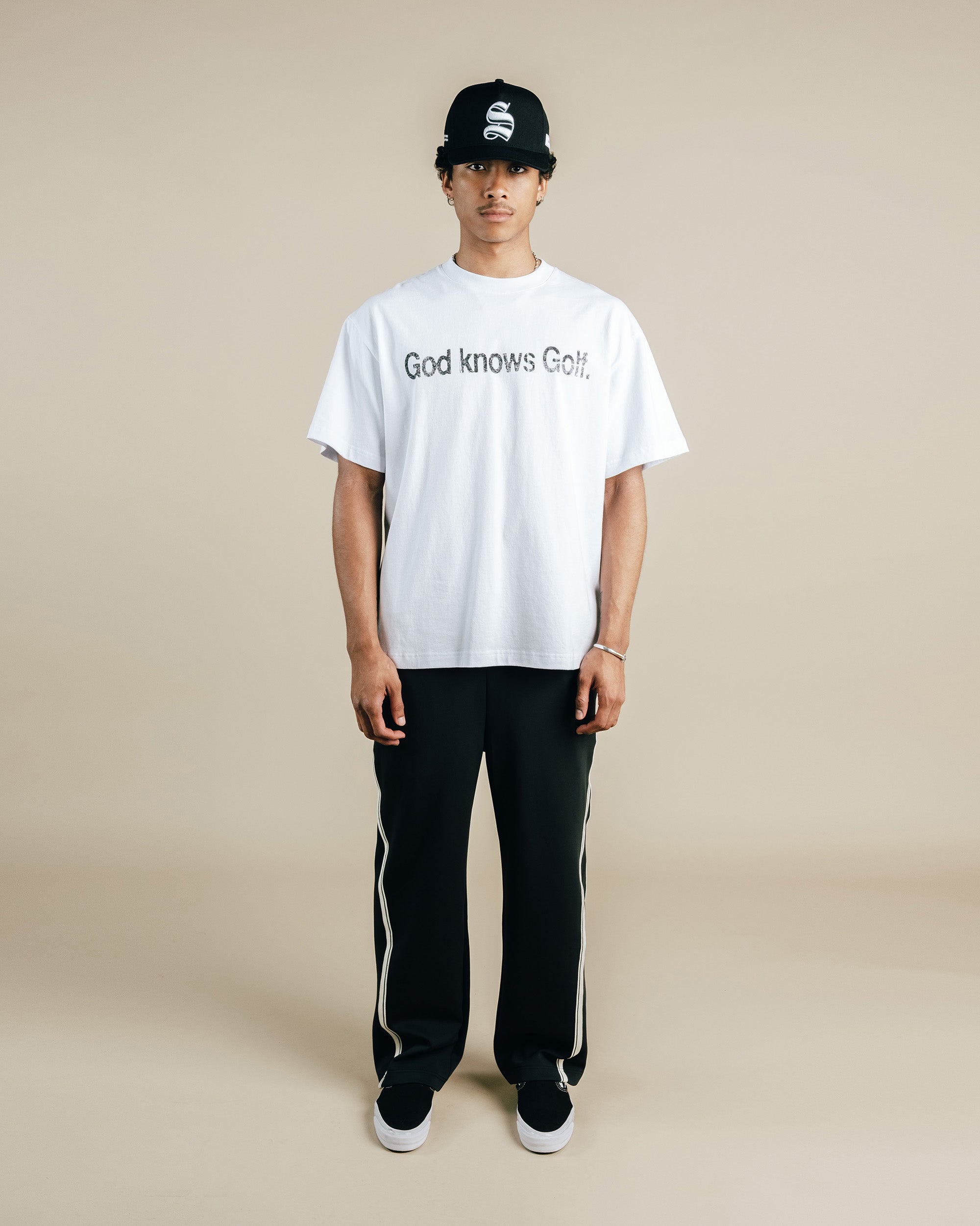 Person wearing a white t-shirt with text and black pants on a beige background