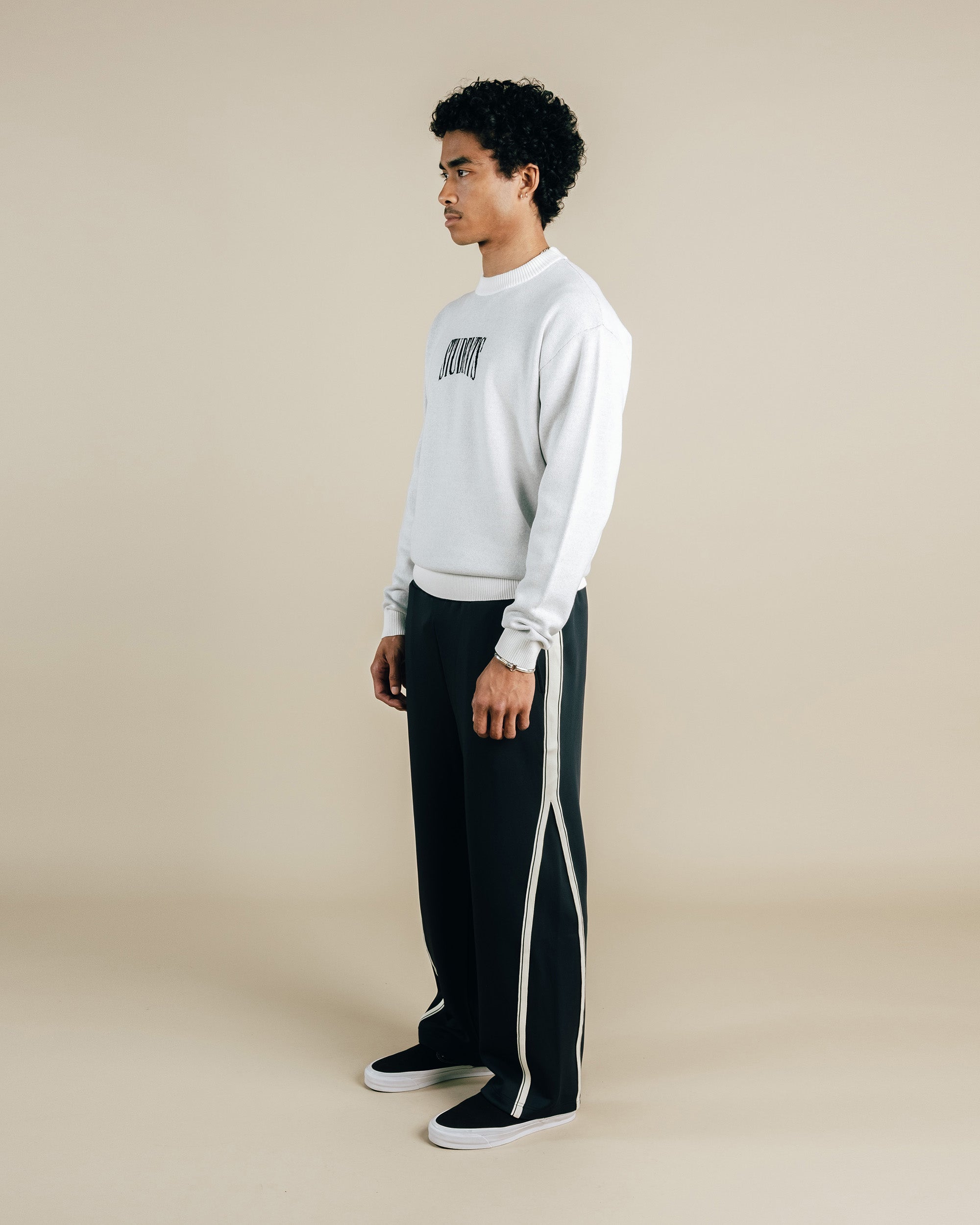 Person wearing a light gray sweatshirt and black pants with white stripes on a beige background