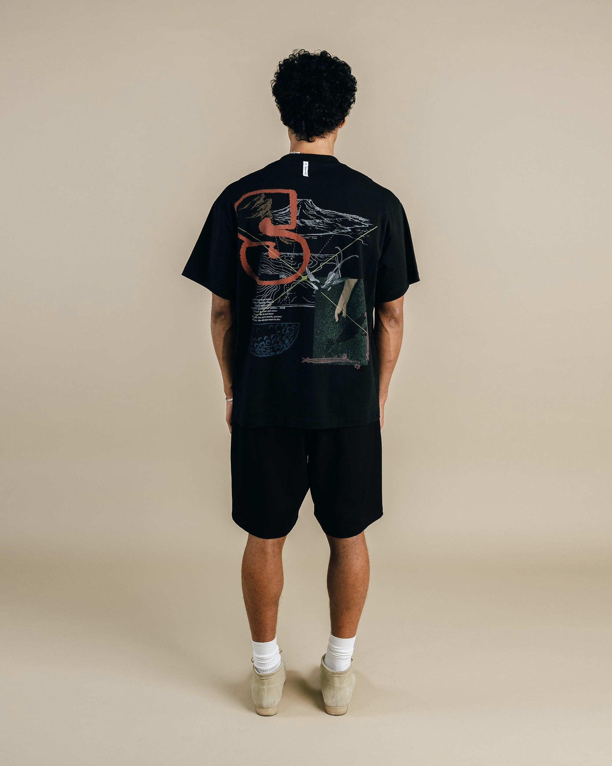 Person wearing a black t-shirt with a design on the back against a beige background