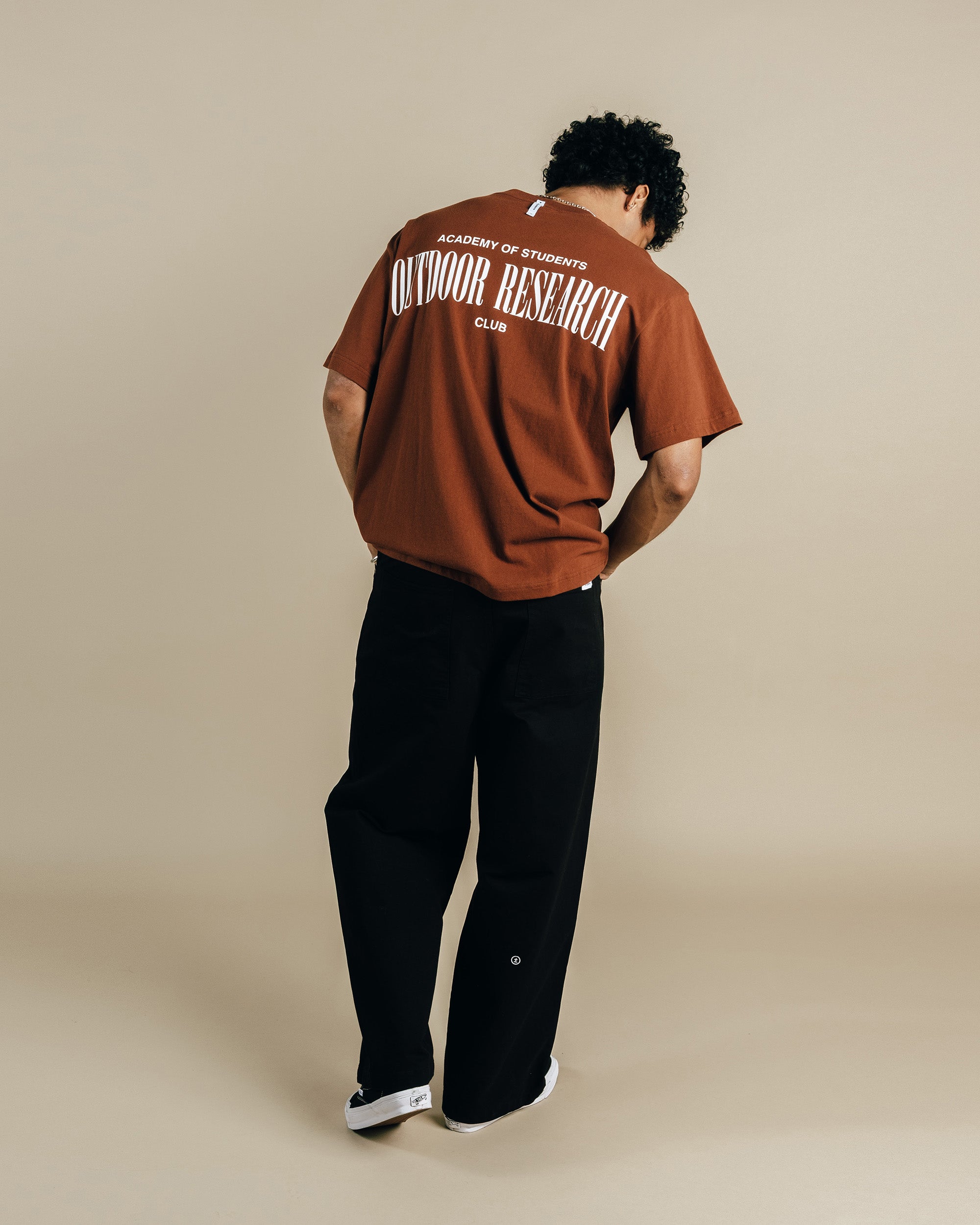 Person wearing a brown 'Outdoor Research' t-shirt on a beige background