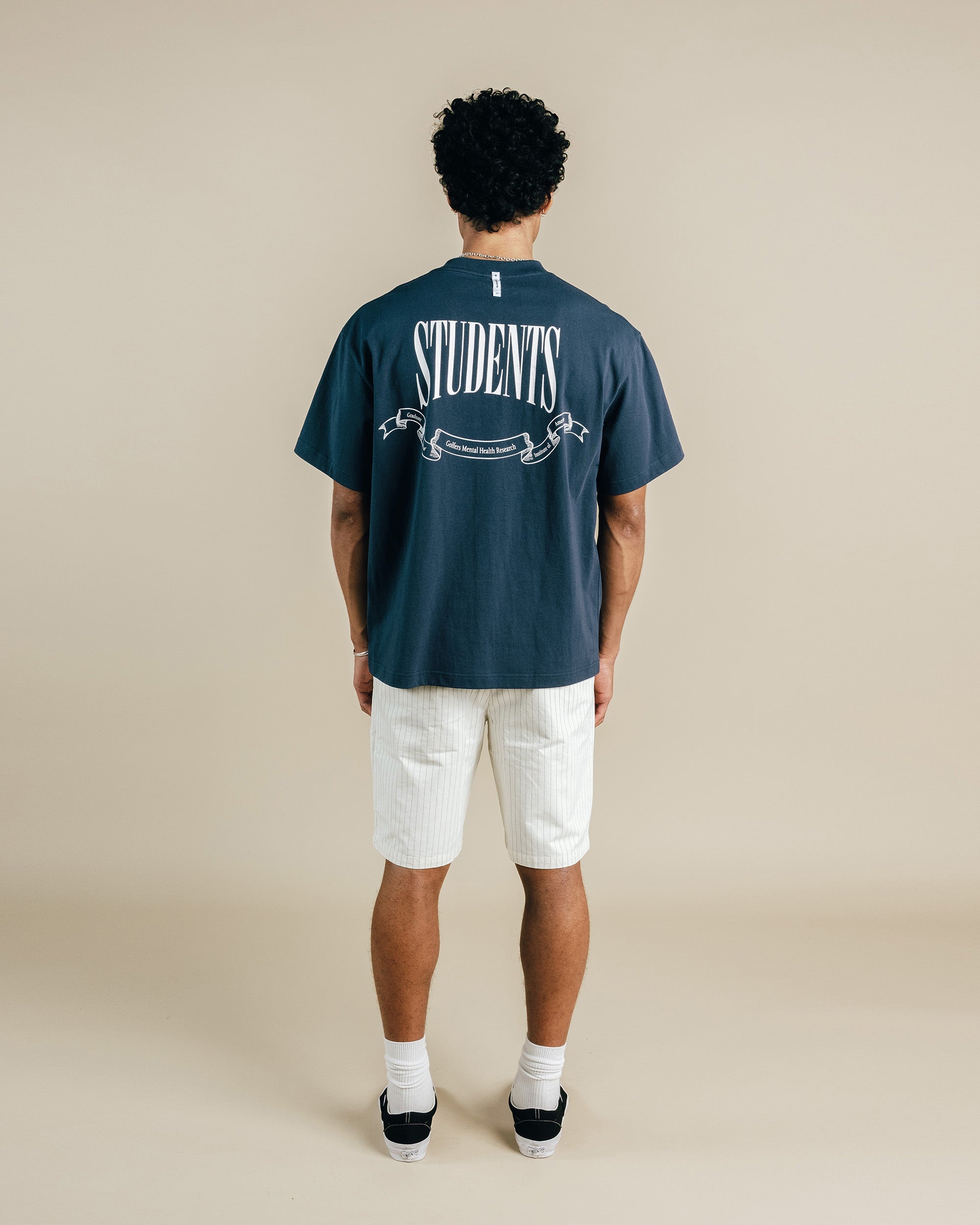 Person wearing a navy blue t-shirt with 'STUDENTS' printed on the back, standing against a beige background.