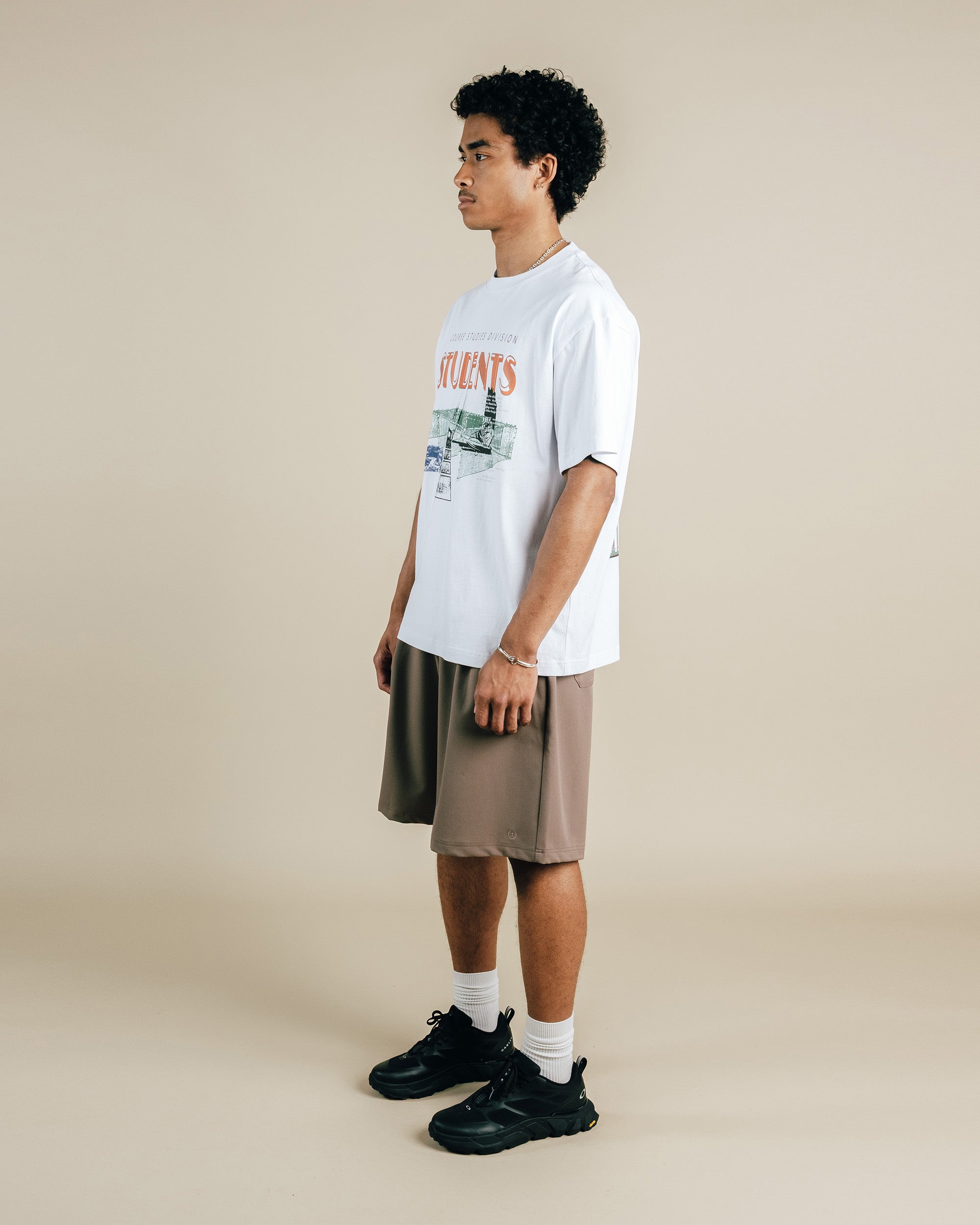 Person wearing a white t-shirt with graphics and brown shorts on a beige background