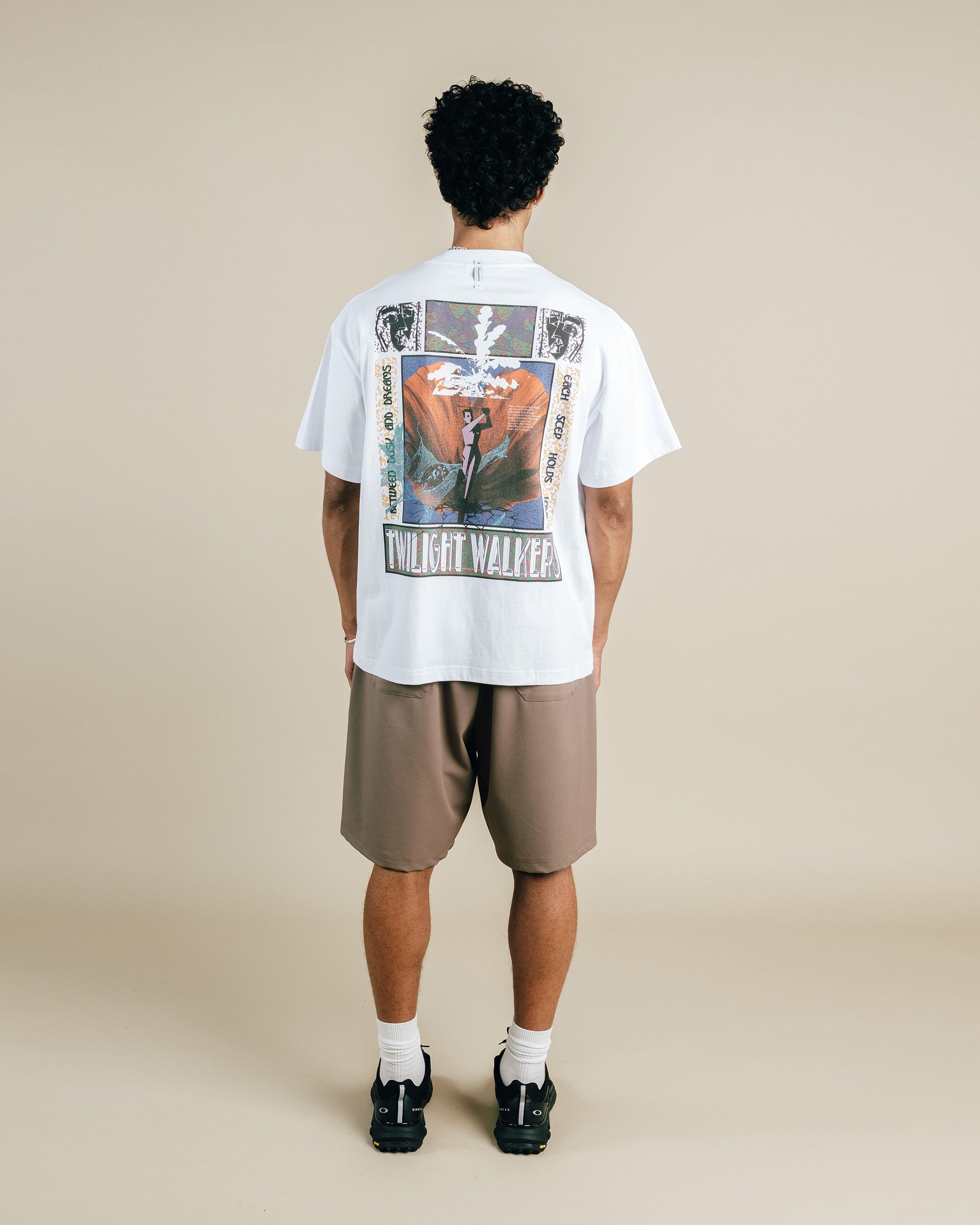 Person wearing a white t-shirt with a graphic design on the back, standing against a beige background