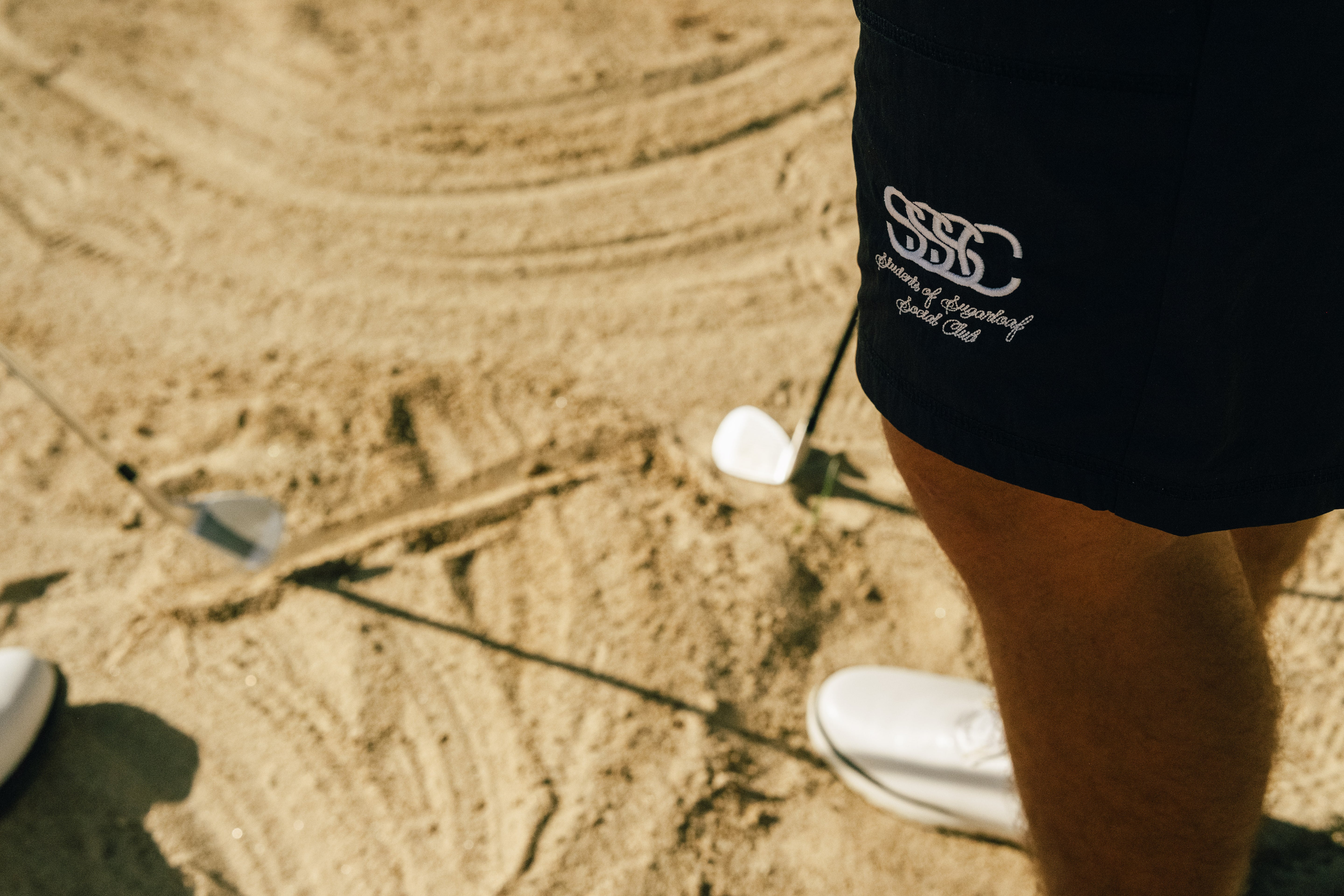 Person wearing a black shorts with a logo on a sandy golf course
