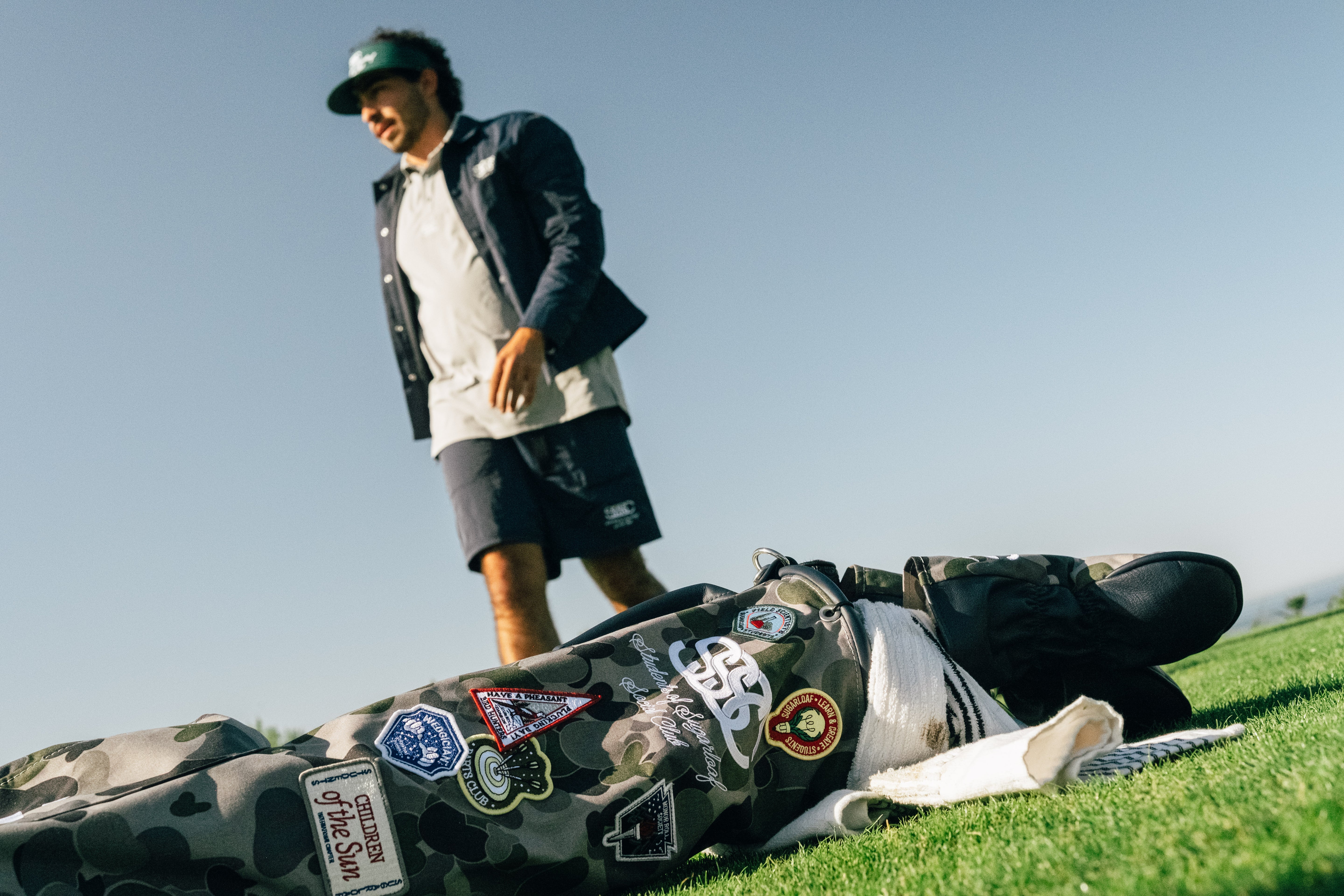 Person standing next to a camouflage vehicle with various stickers on a grassy area.