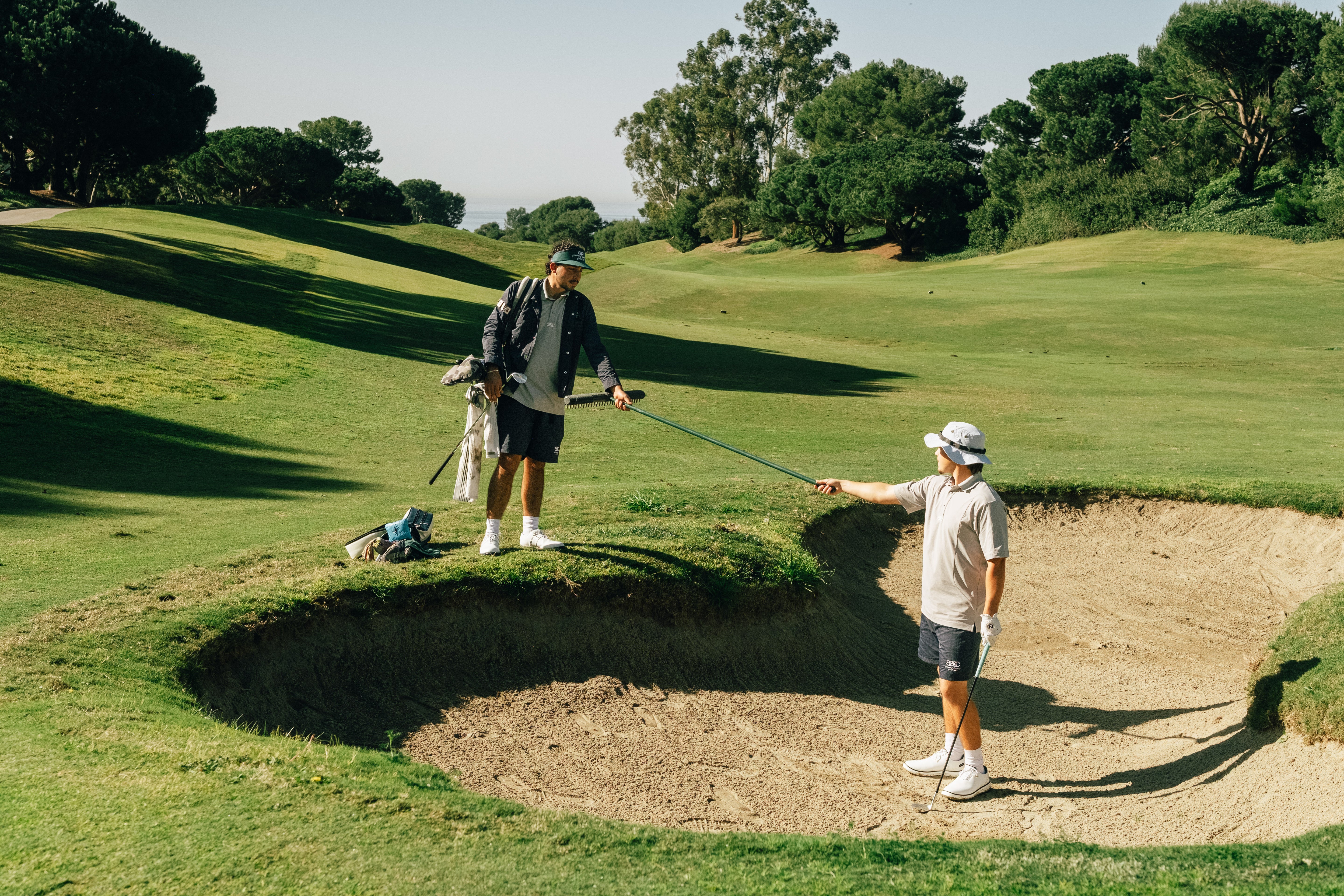 Two golfers on a golf course with one approaching a sand trap.
