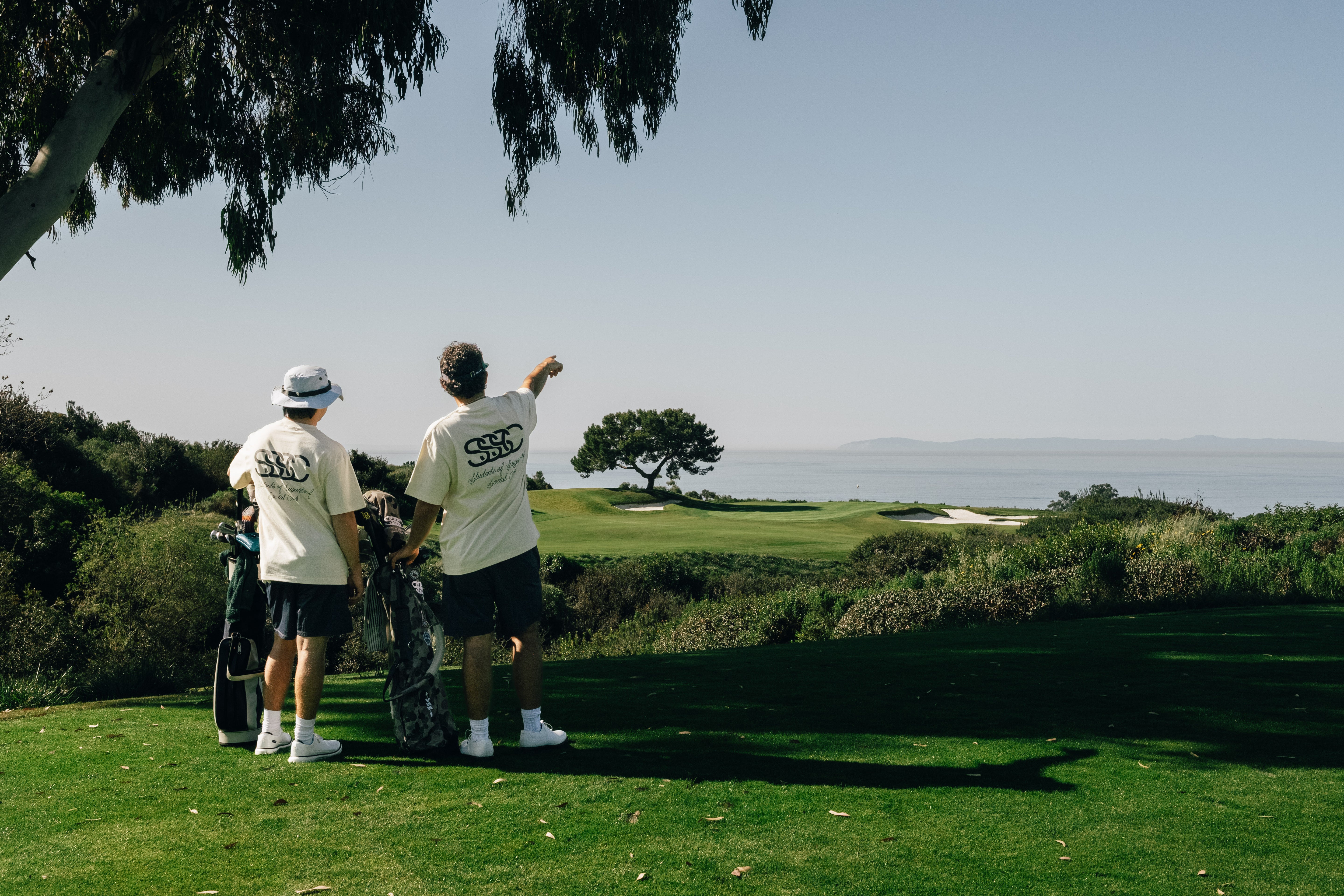 Two golfers on a green course with a scenic view of the ocean.