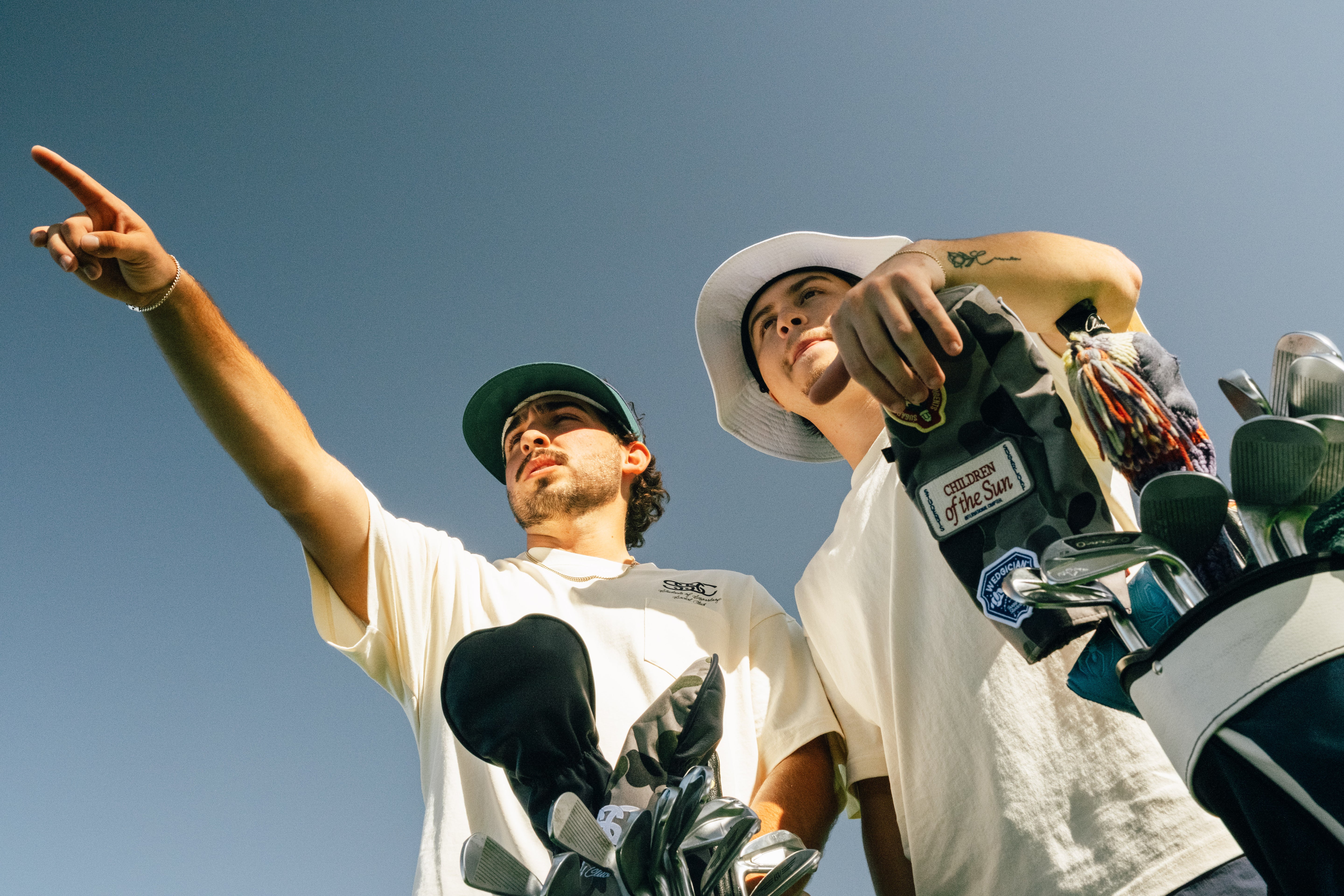 Two individuals holding golf clubs against a clear blue sky