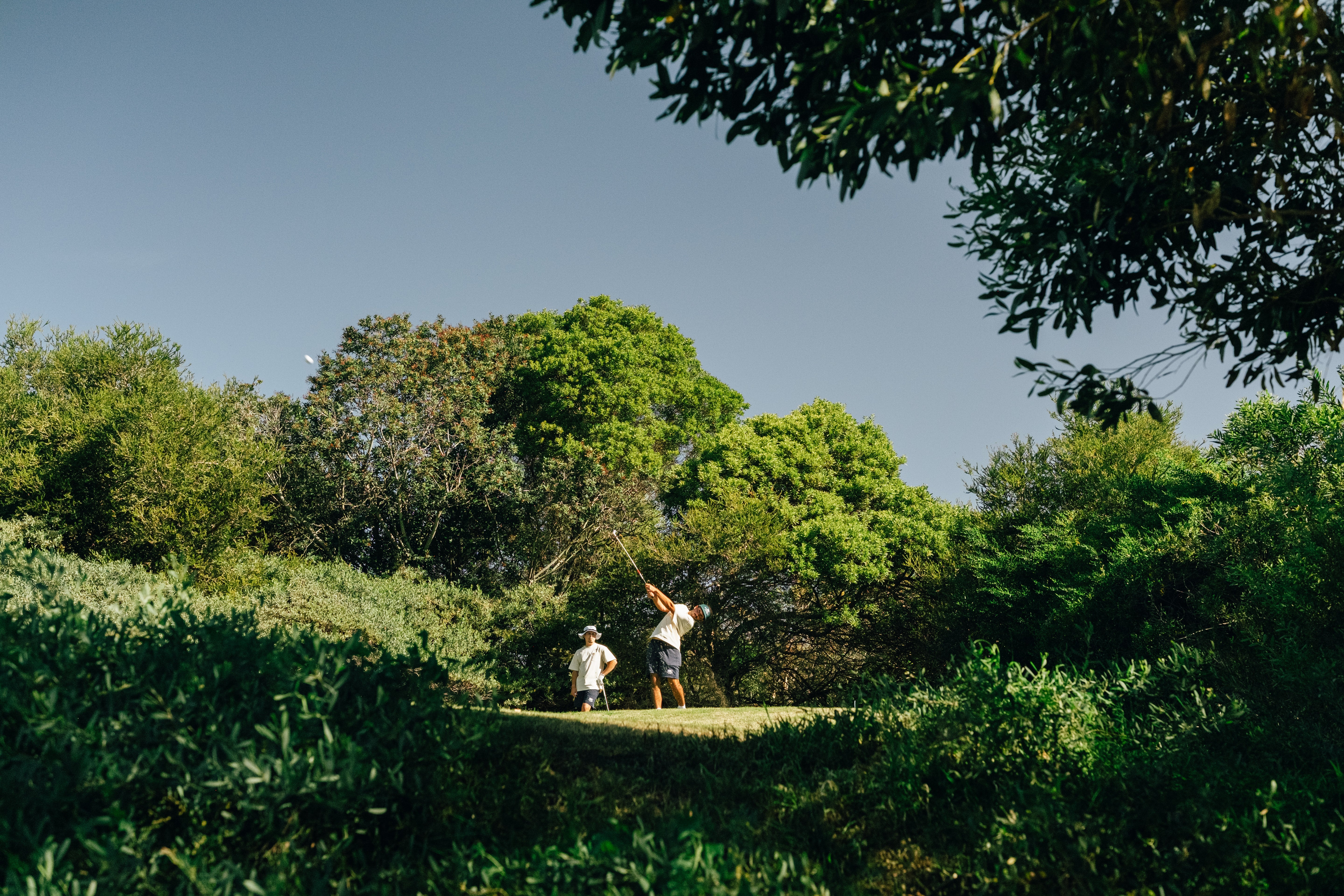 Two people playing golf on a grassy area with trees in the background