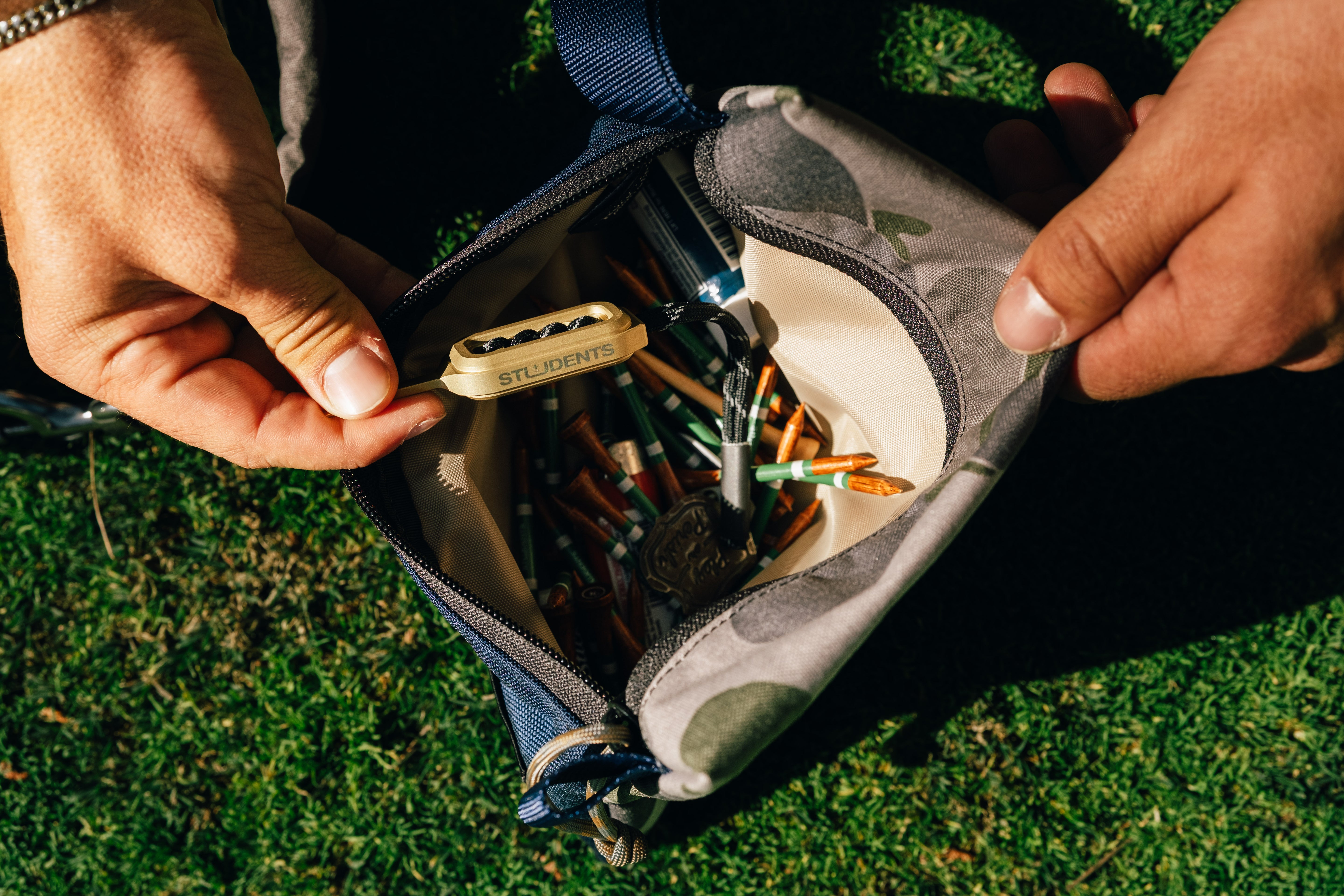Person opening a small pouch containing tools on grass