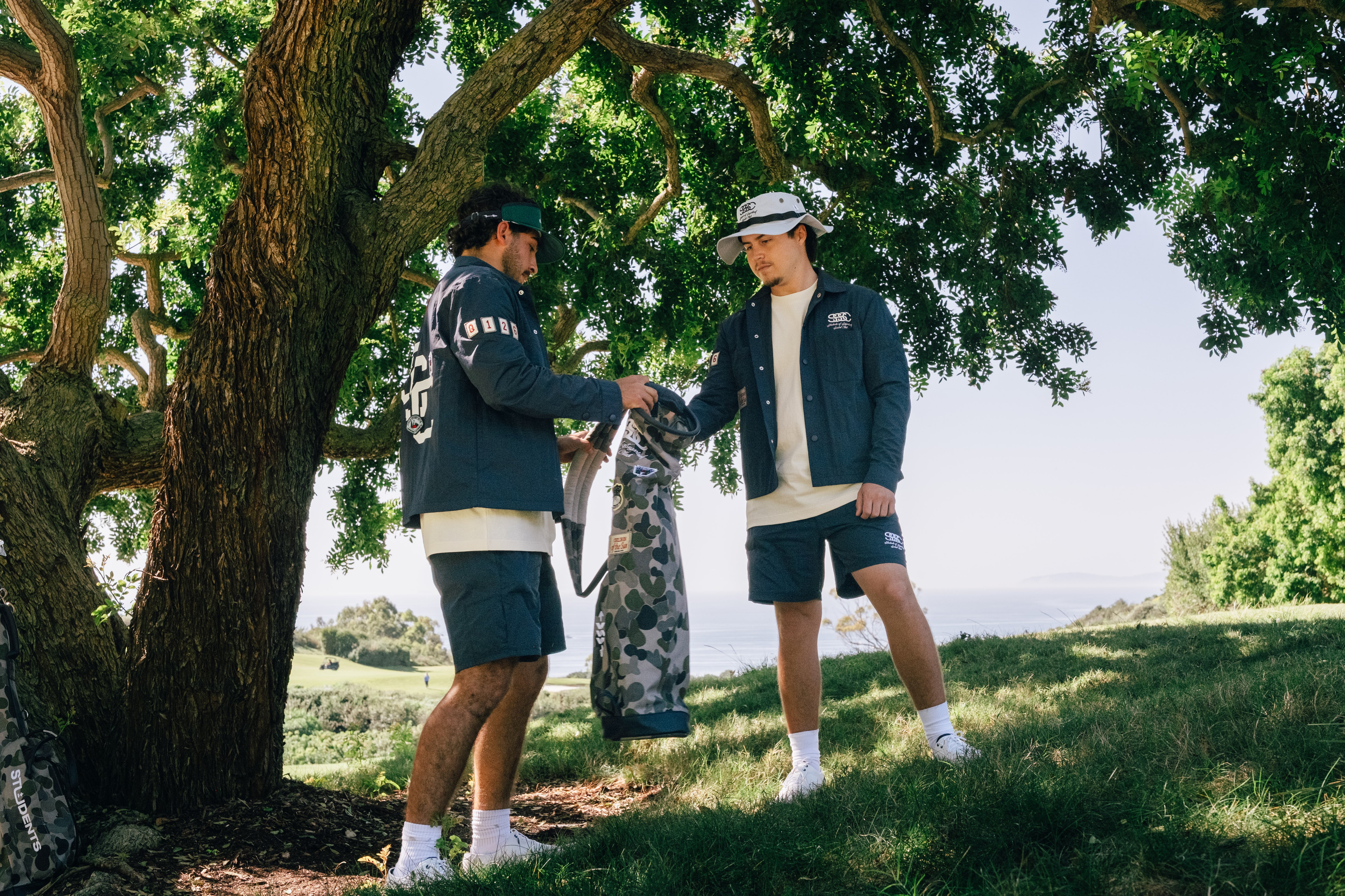 Two people in outdoor clothing standing under a tree with a scenic background
