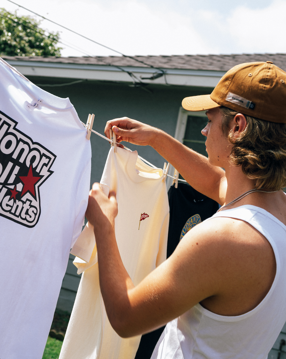 Person hanging t-shirts on a clothesline with a house in the background