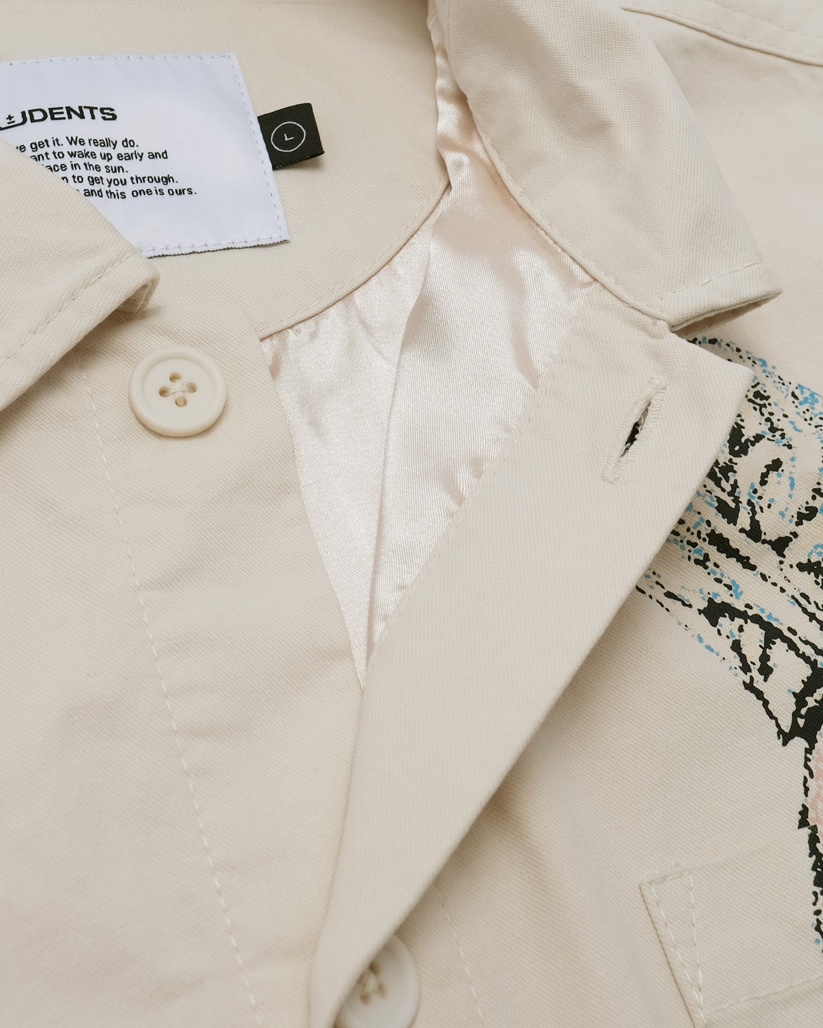 Close-up of a beige coat with a button and a label on a patterned fabric background