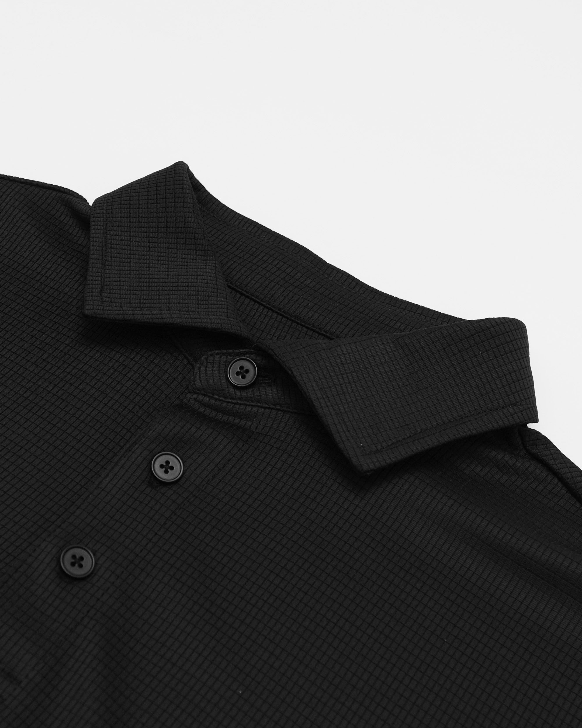 Close-up of a black textured shirt with buttons on a light gray background