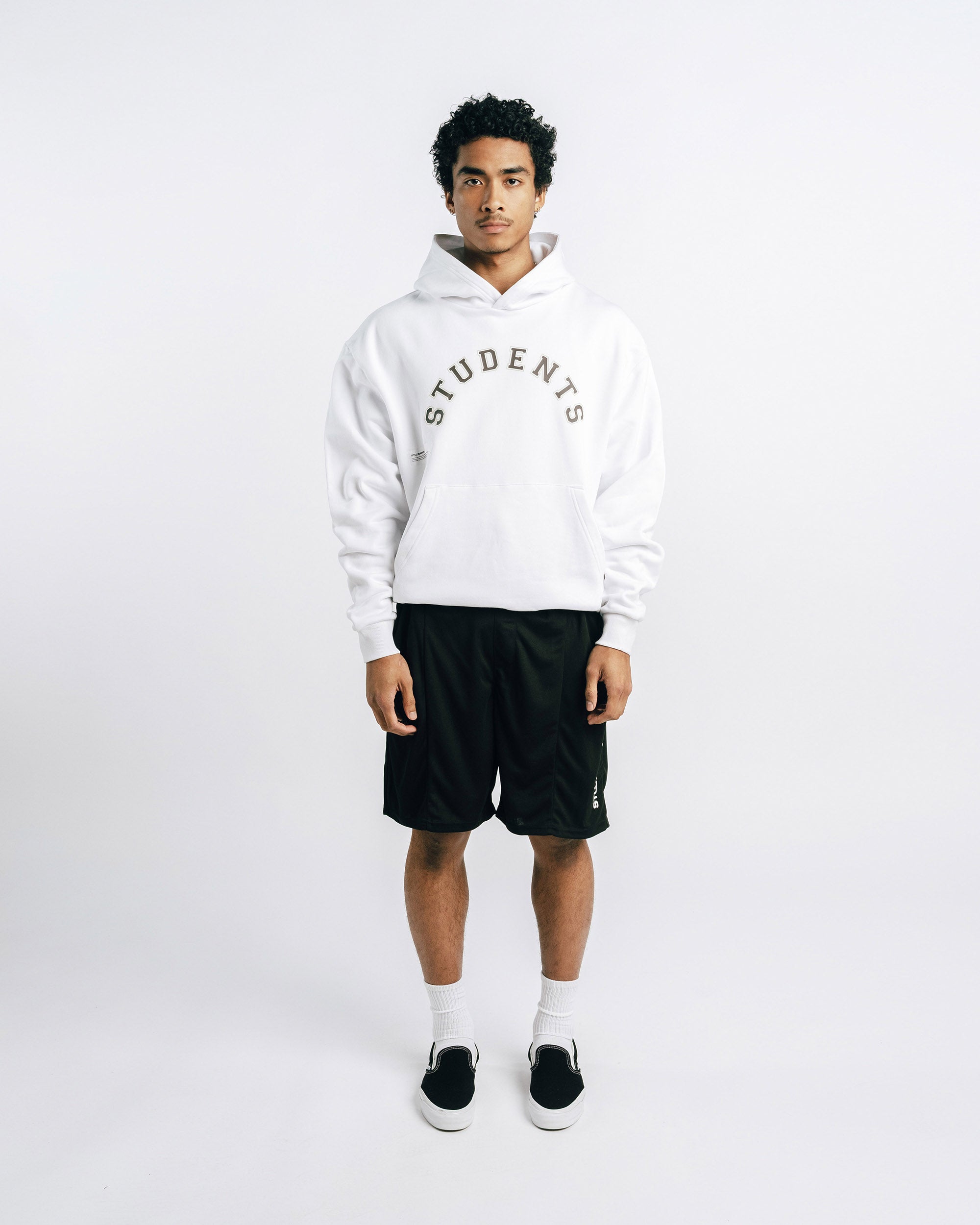 Person wearing a white hoodie with 'STUDENTS' text, black shorts, and black shoes on a white background