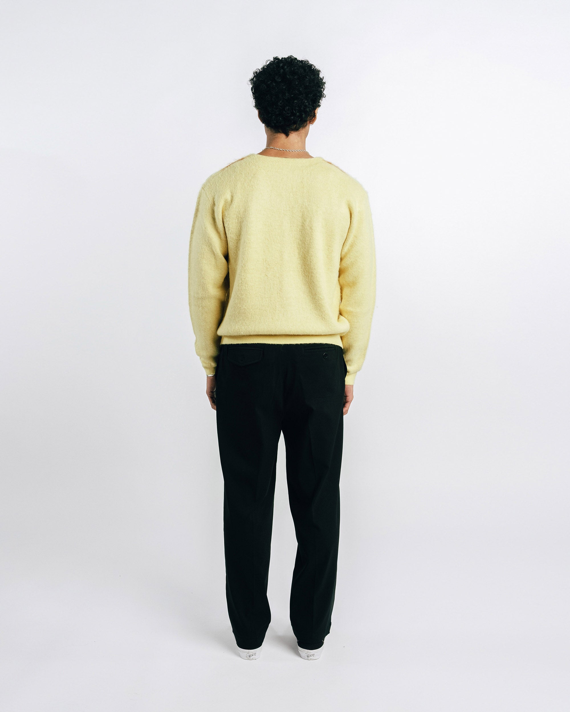 Person wearing a light yellow sweater and black pants on a white background