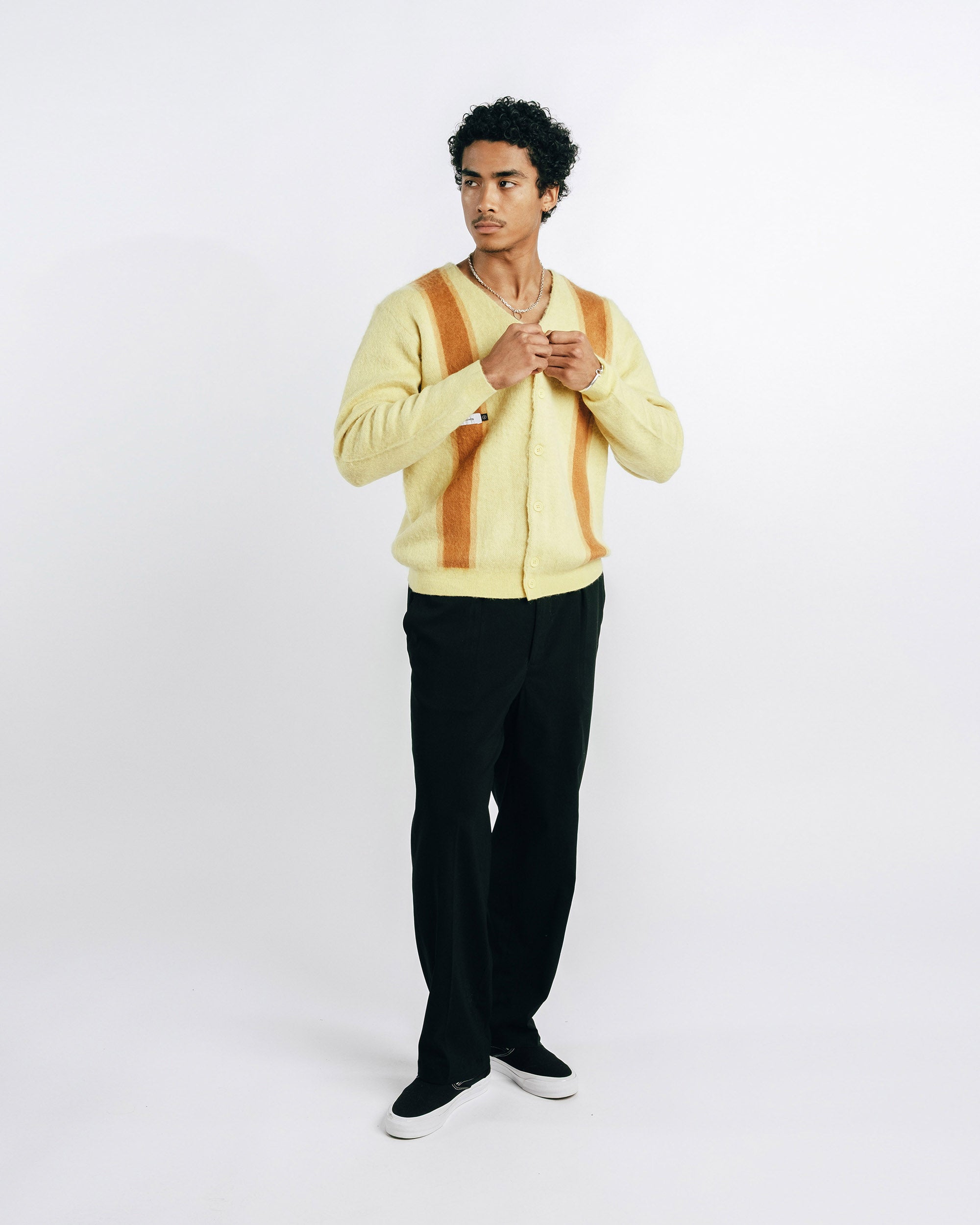 Man wearing a light yellow cardigan with brown stripes on a white background