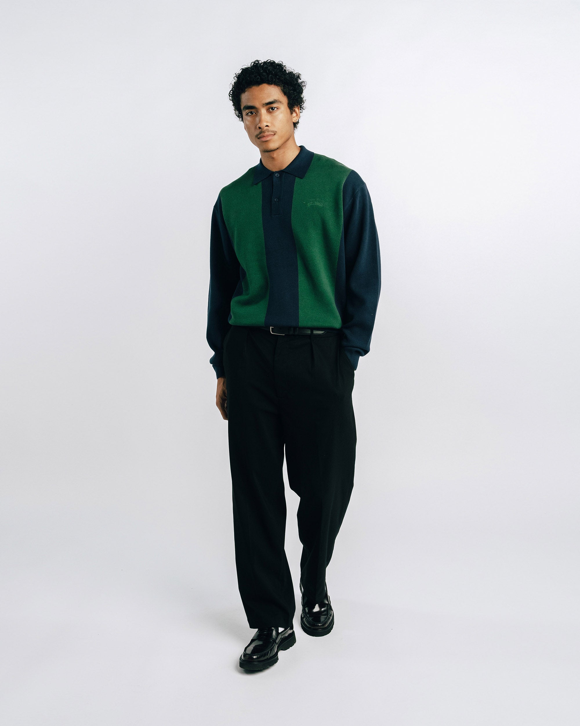 Man wearing a green and black shirt with black pants on a white 