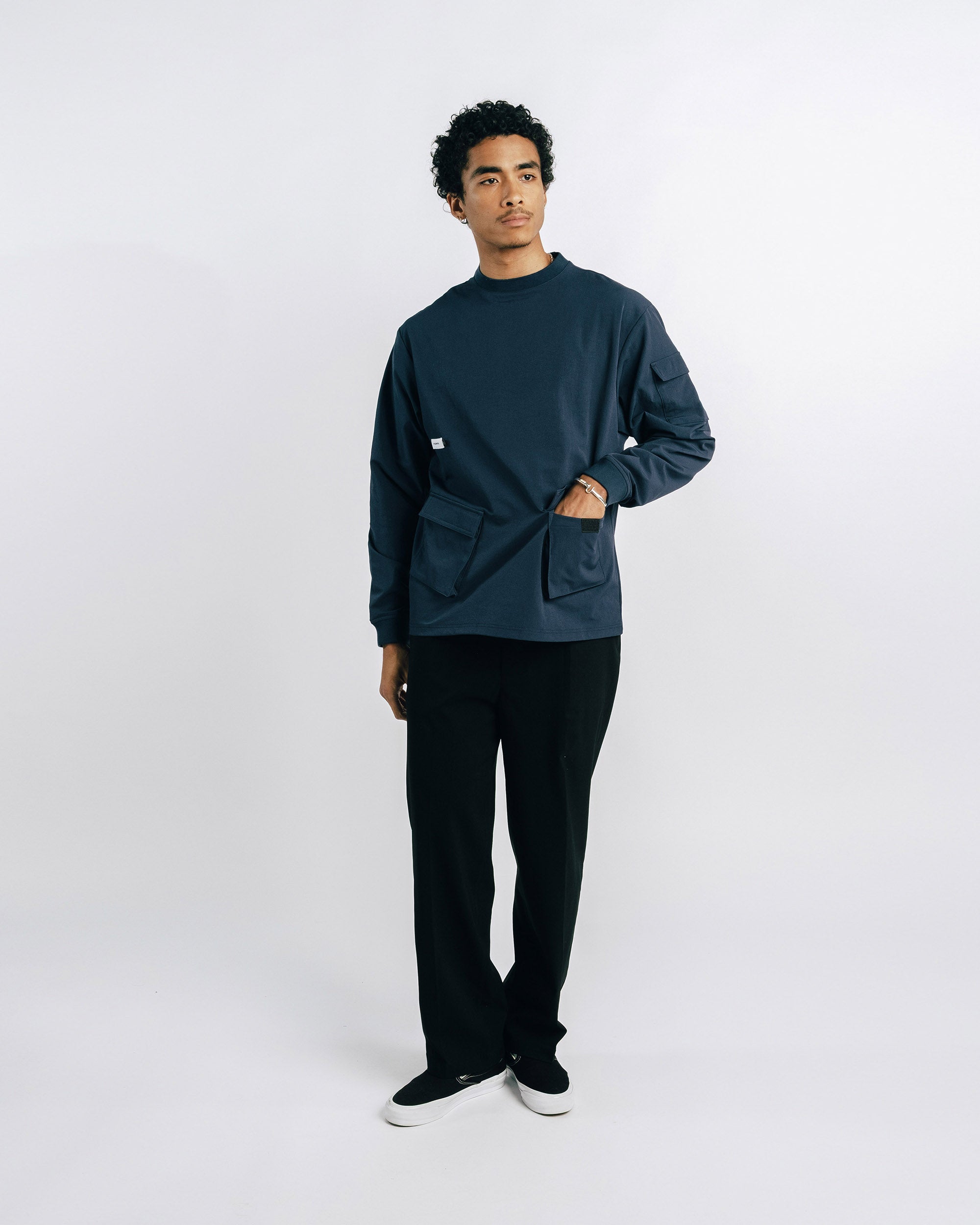 Person wearing a dark green sweater and black pants on a white background