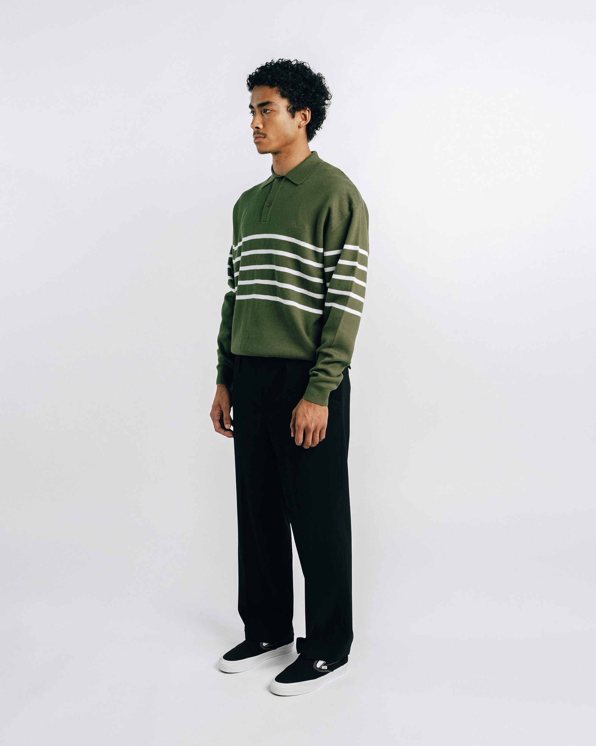 Person wearing a green and white striped sweater with black pants on a white background