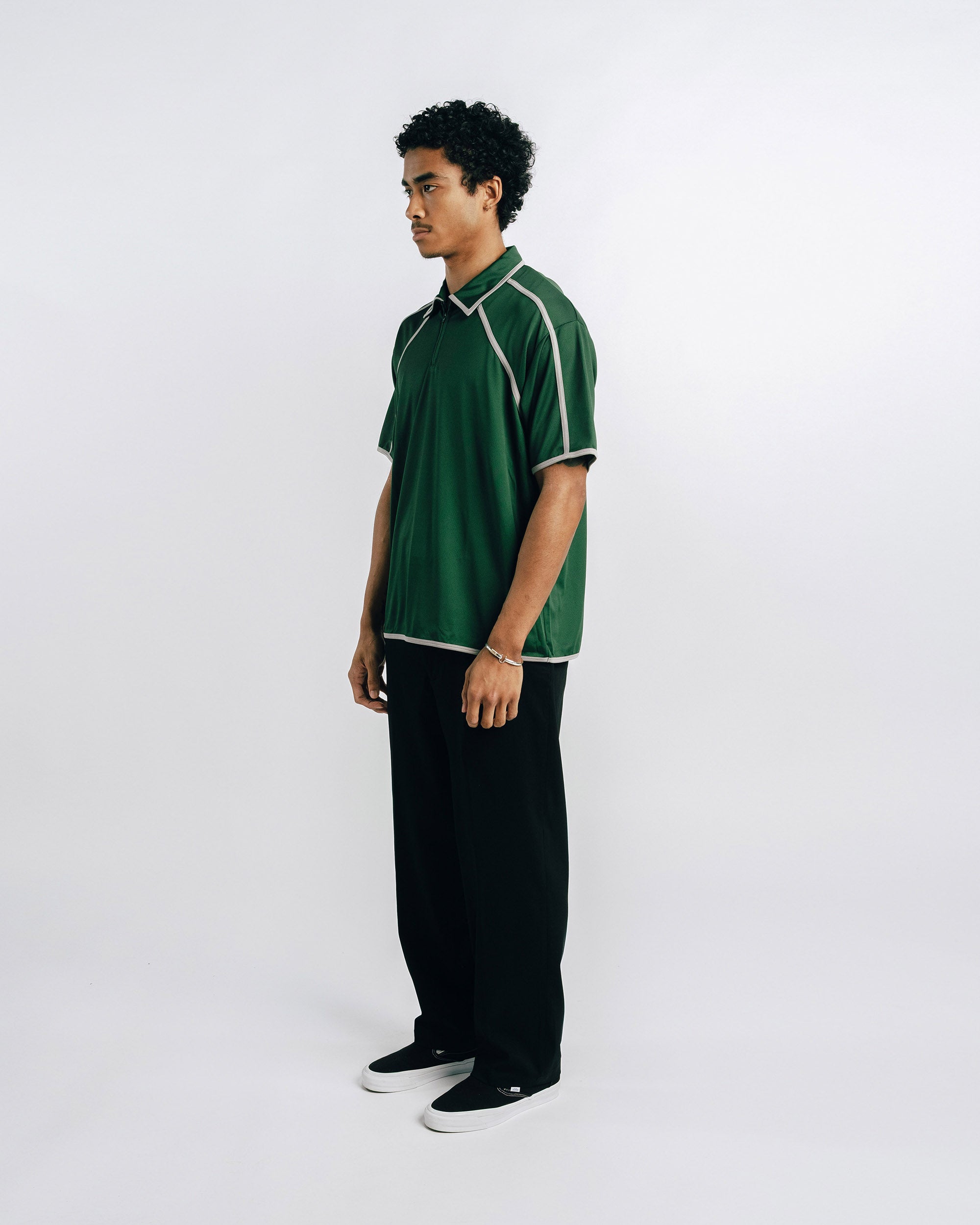 Person wearing a green polo shirt and black pants on a white background