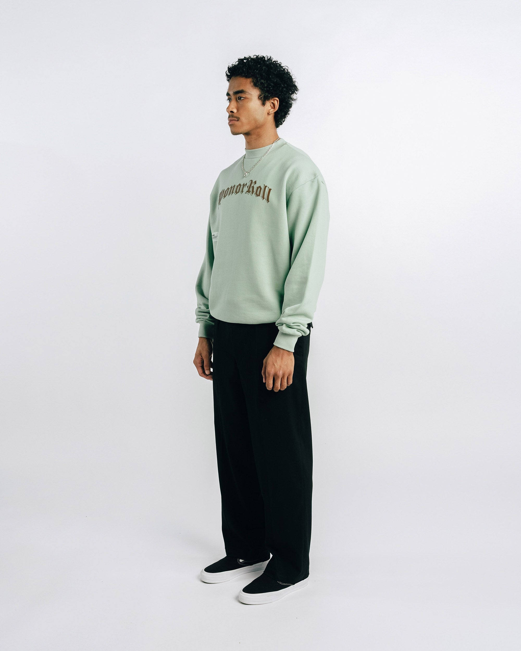 Person wearing a light green sweater with text and black pants on a white background