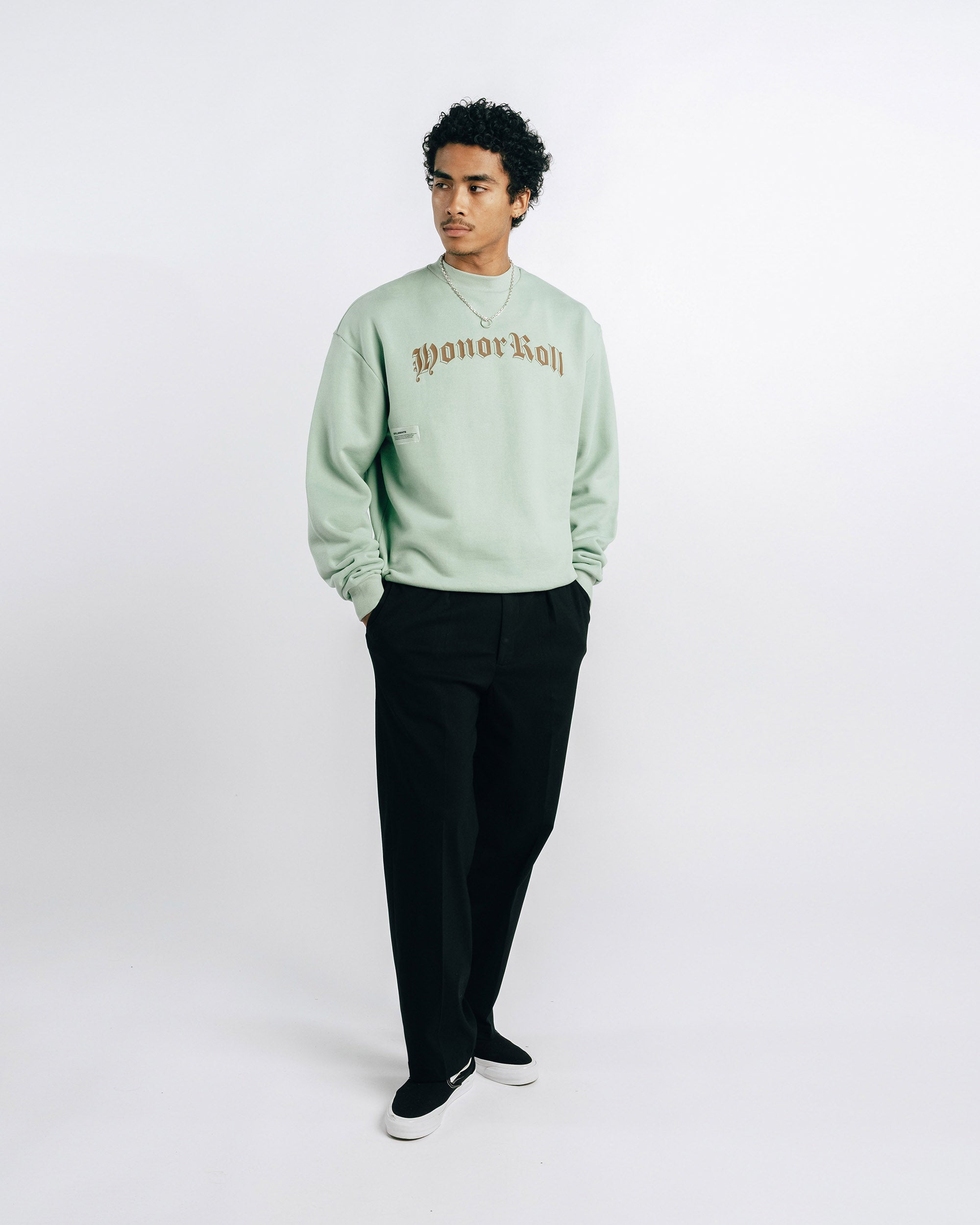 Person wearing a light green sweatshirt with text and black pants on a white background