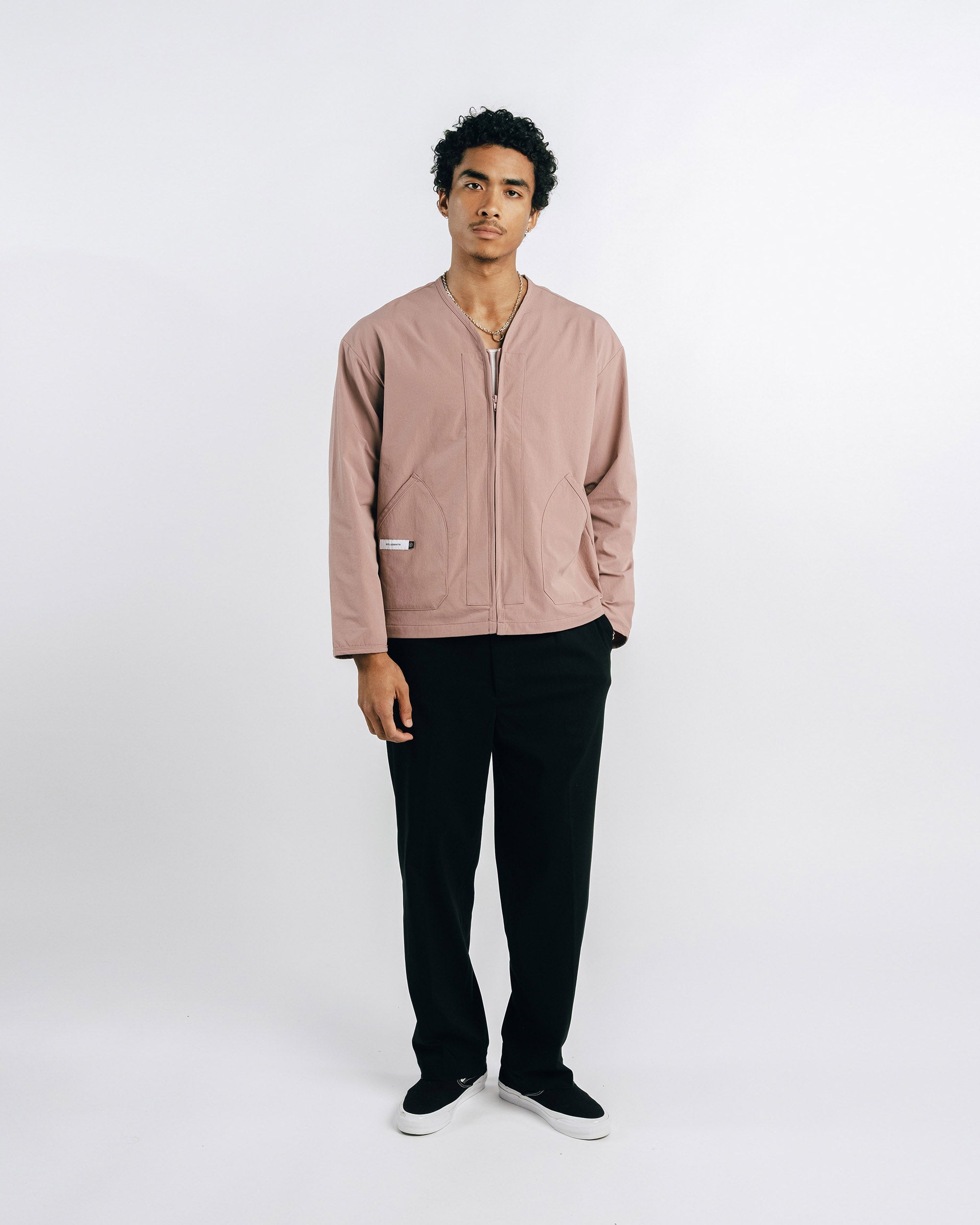 Man wearing a light pink jacket and black pants on a white background