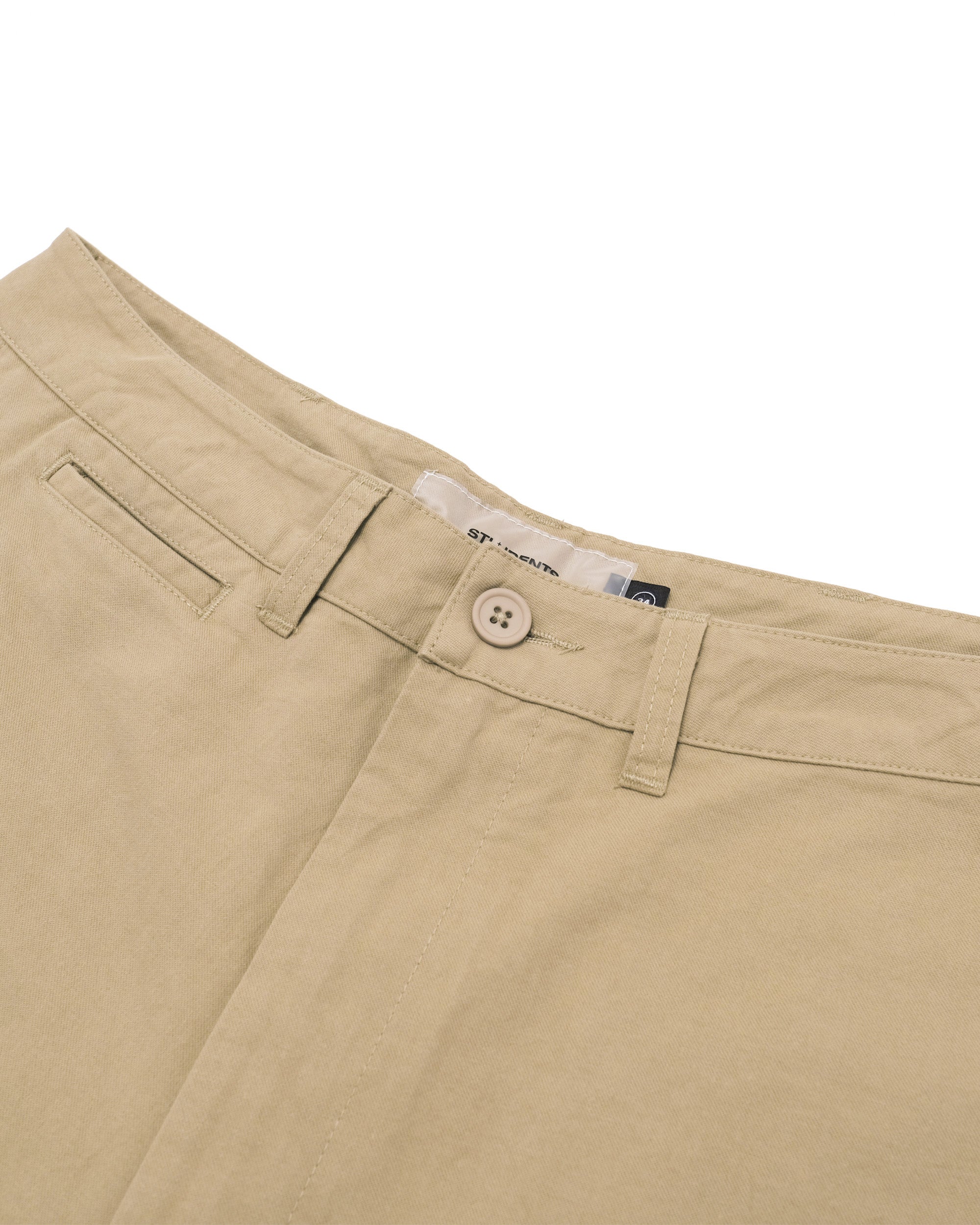 Close-up of beige pants with a button and brand label on a white background