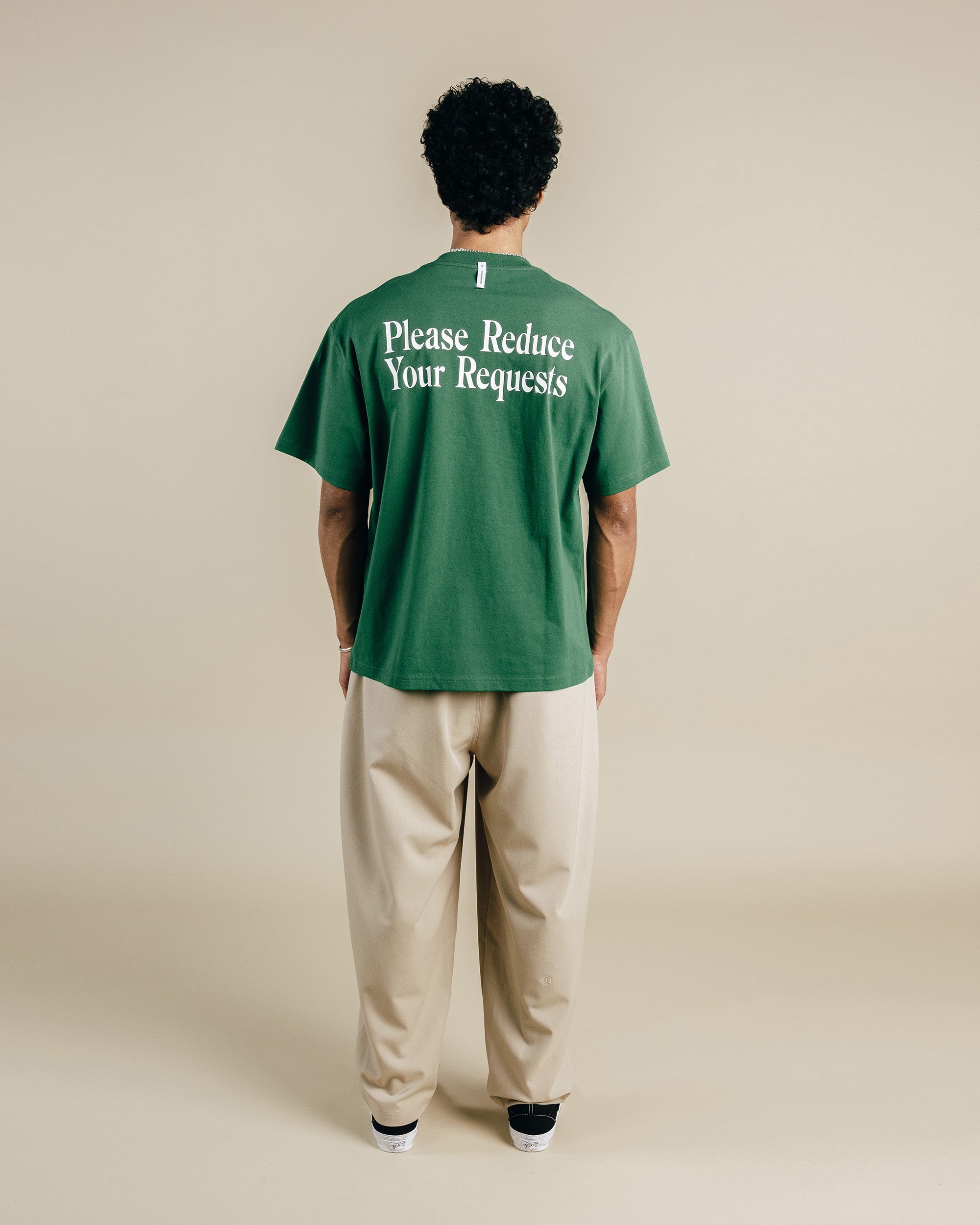 Person wearing a green t-shirt with text on the back, standing against a plain background