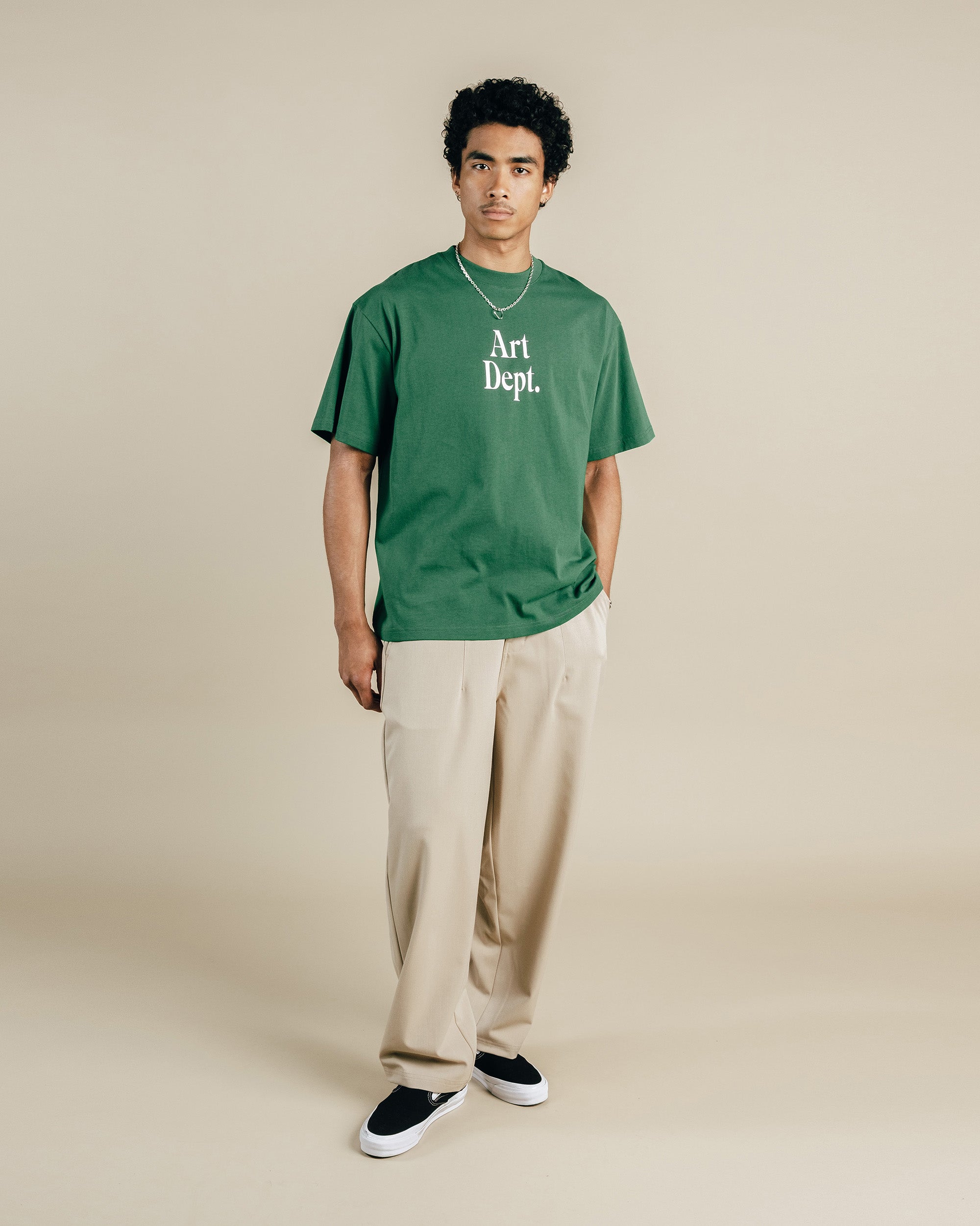 Man wearing a green 'Art Dept.' t-shirt and beige pants on a beige background