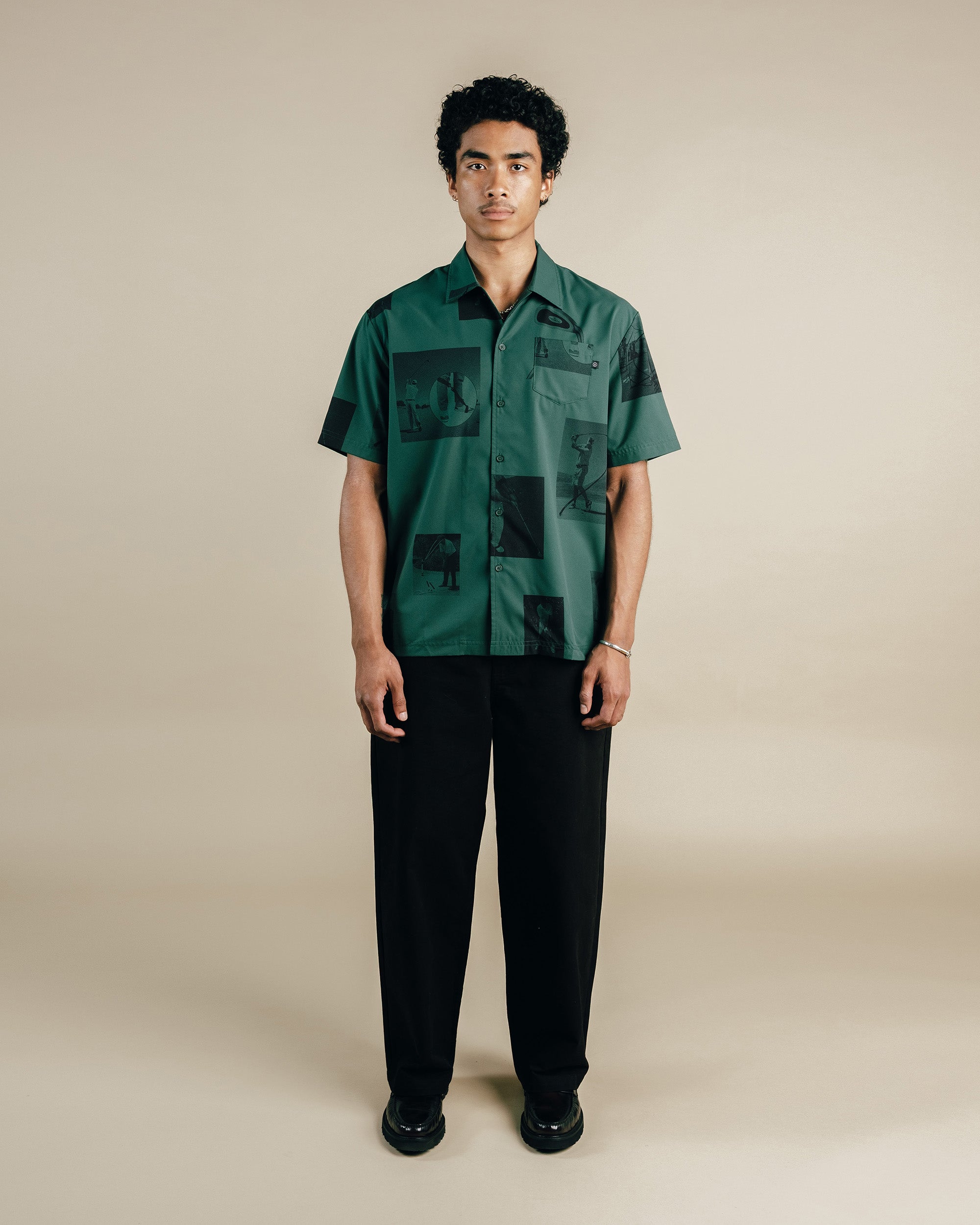 Man wearing a green patterned shirt and black pants on a beige background