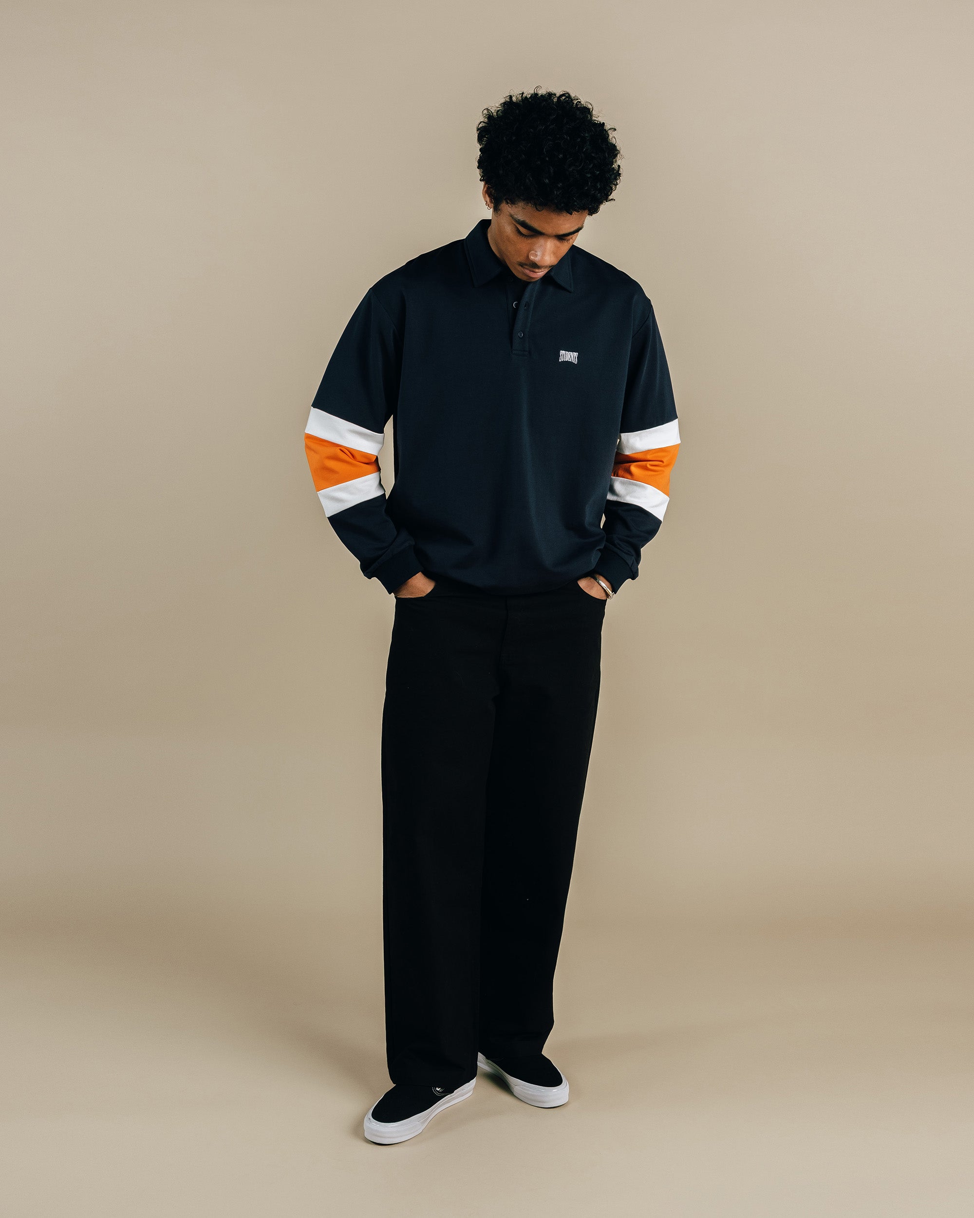 Person wearing a black and orange striped shirt with a logo on a beige background