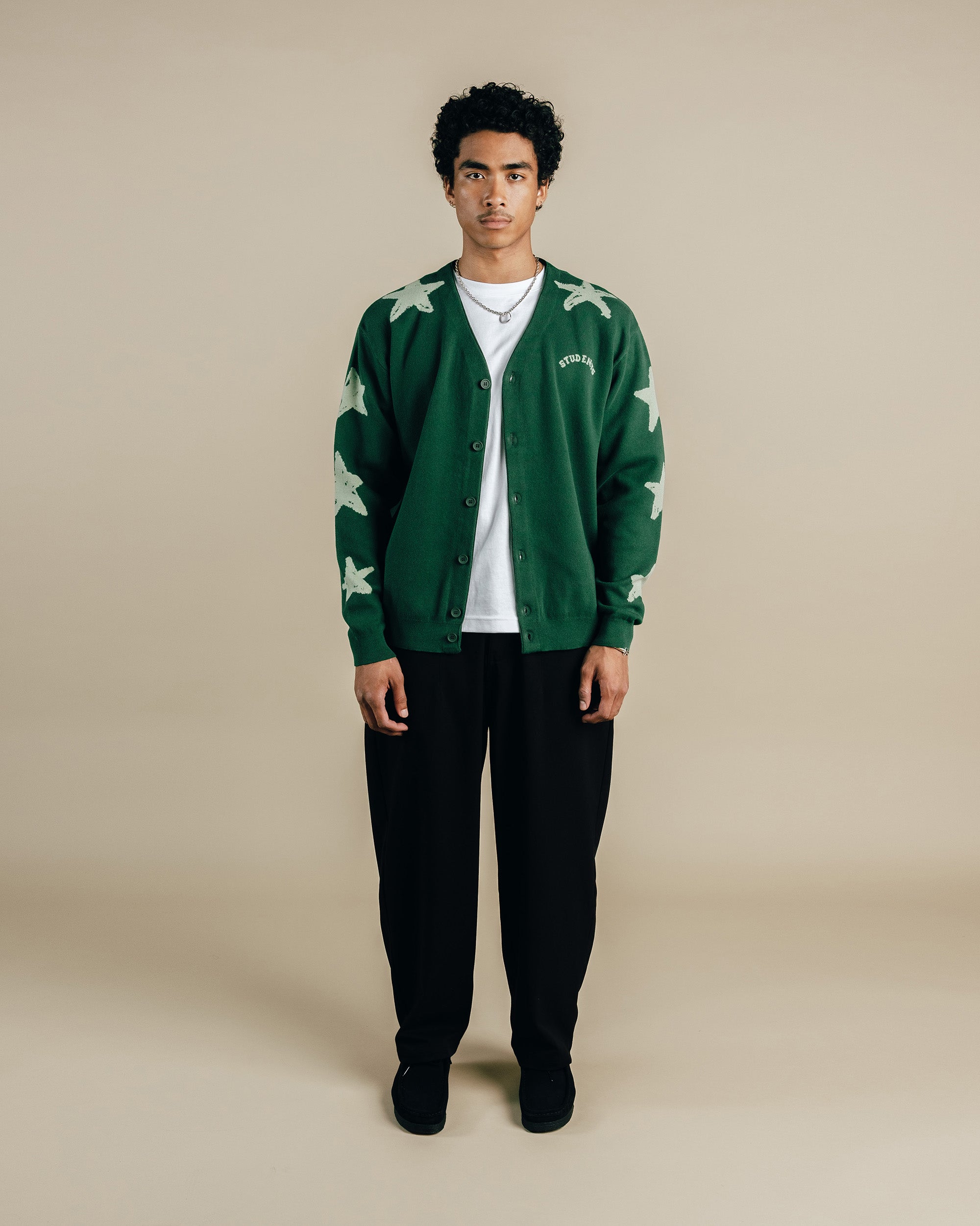 Person wearing a green cardigan with white star patterns on a beige background