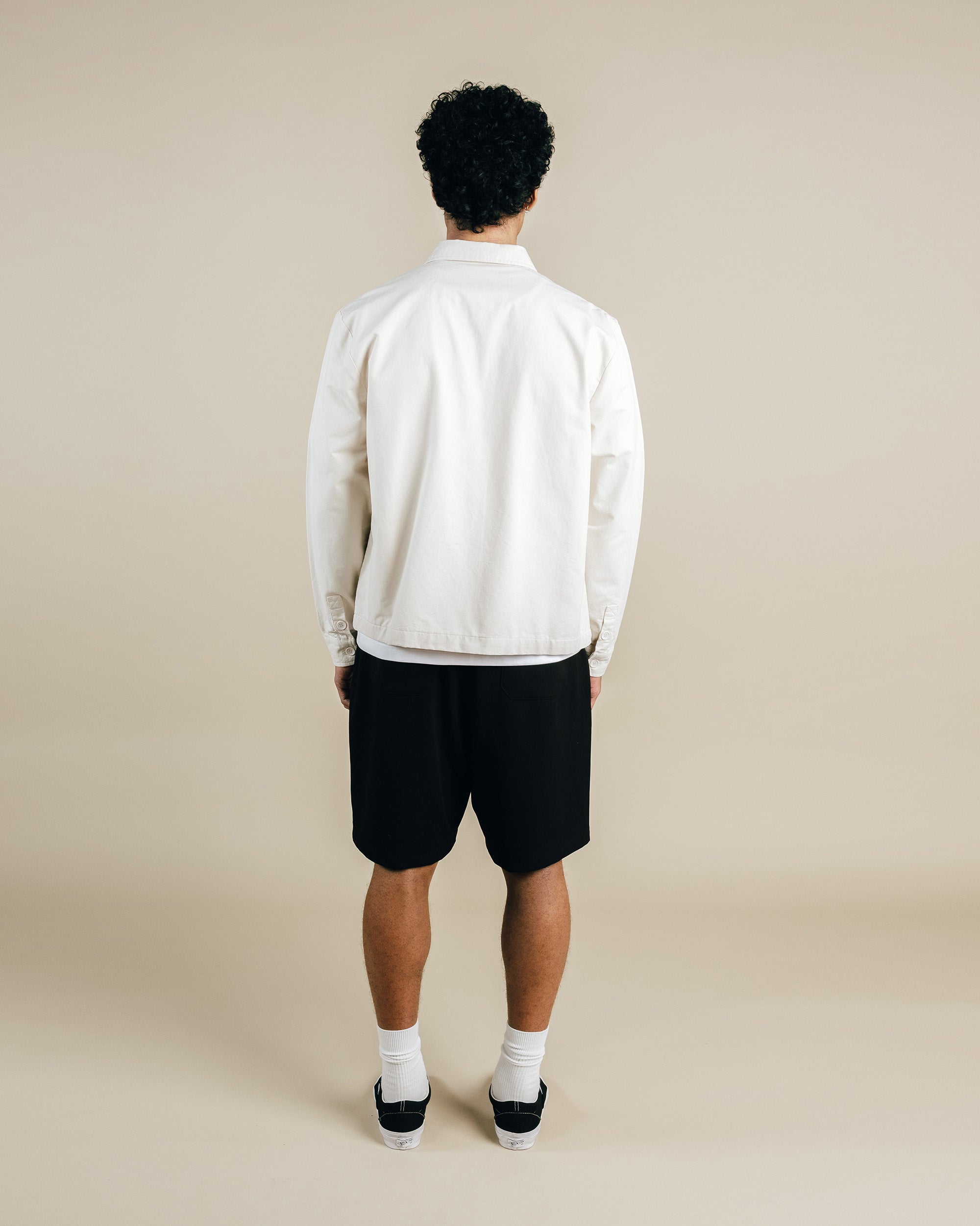 Person wearing a white jacket and black shorts on a beige background