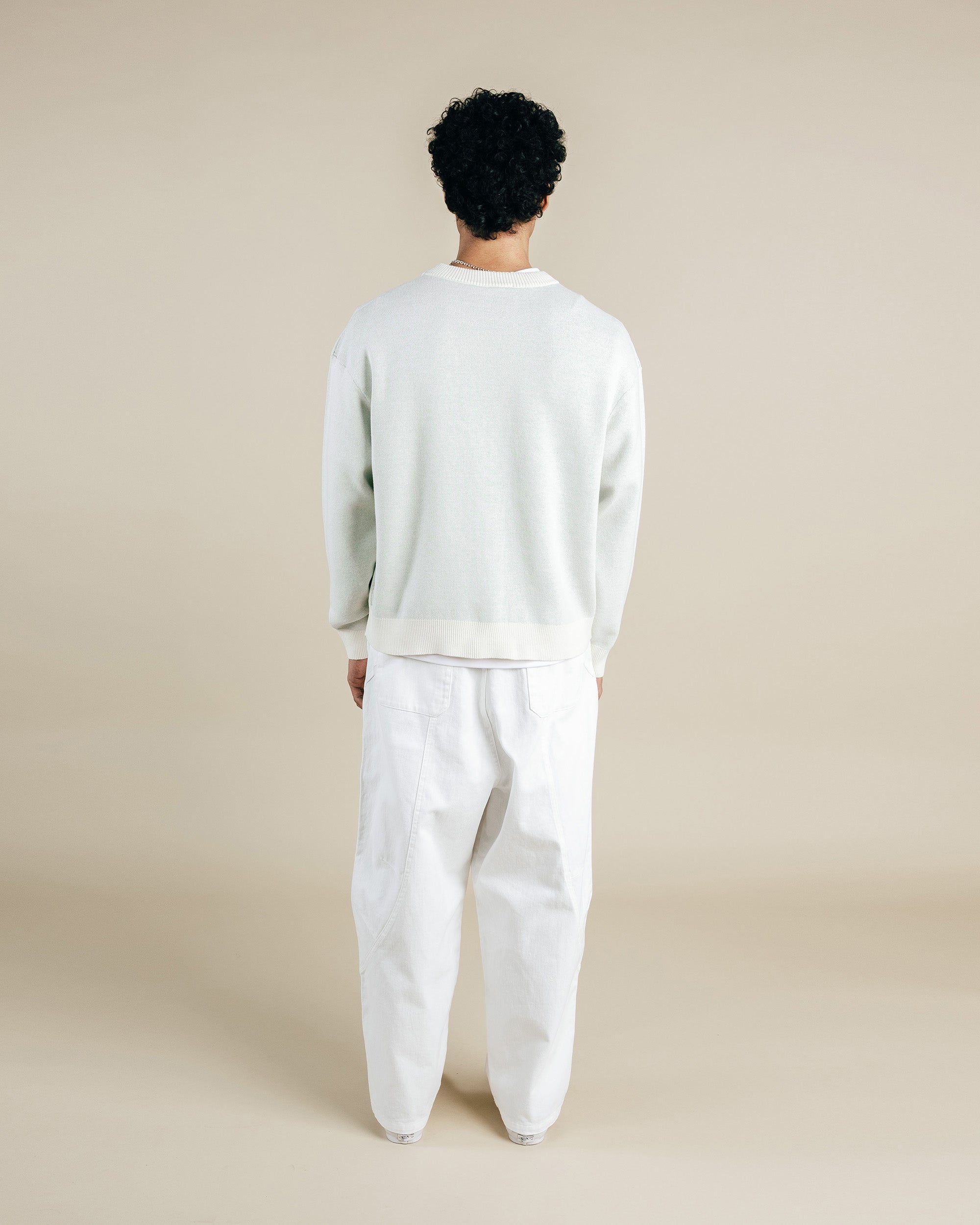 Person wearing a light gray sweater and white pants on a beige background