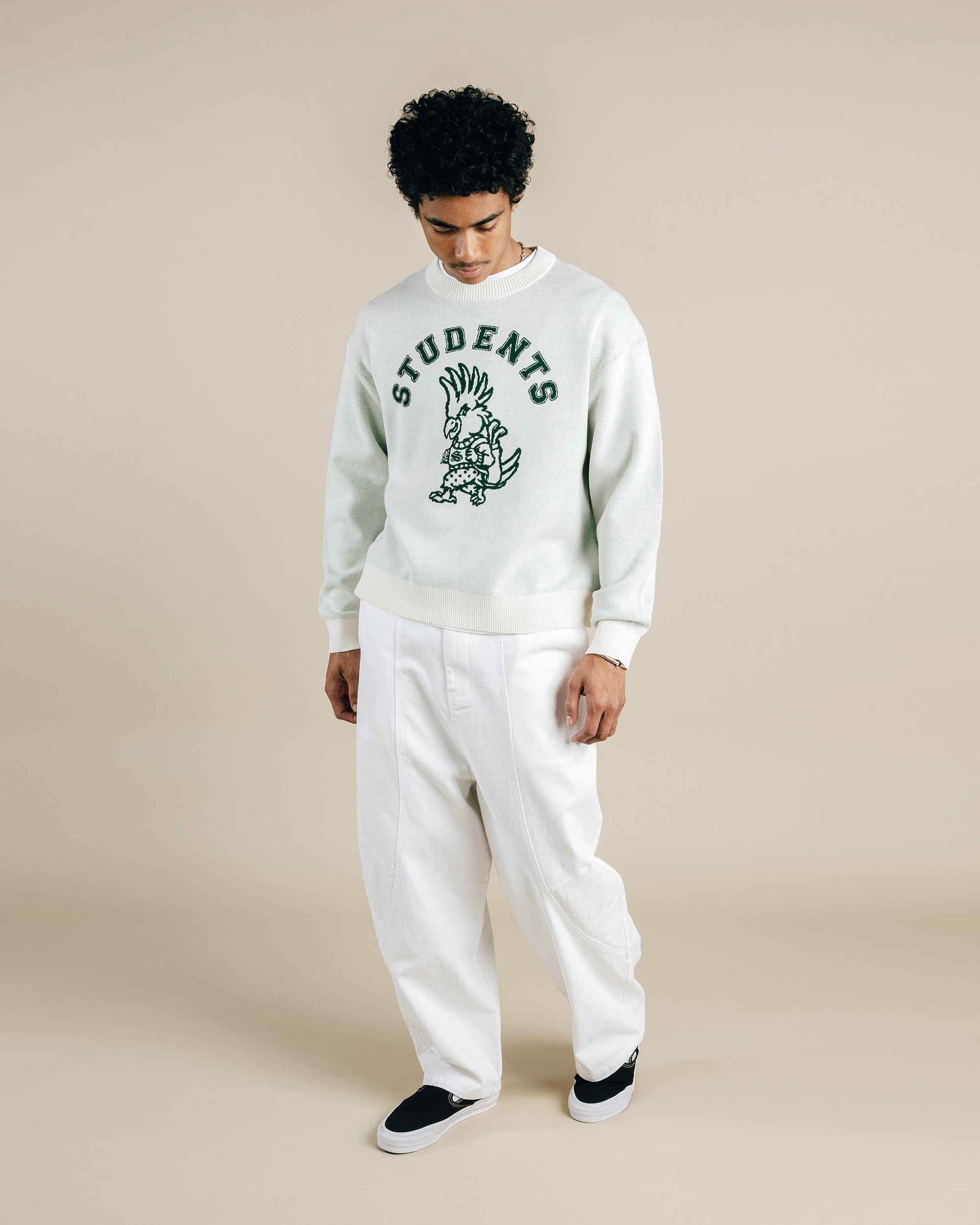 Person wearing a white sweatshirt with a graphic design and text, paired with white pants on a beige background.