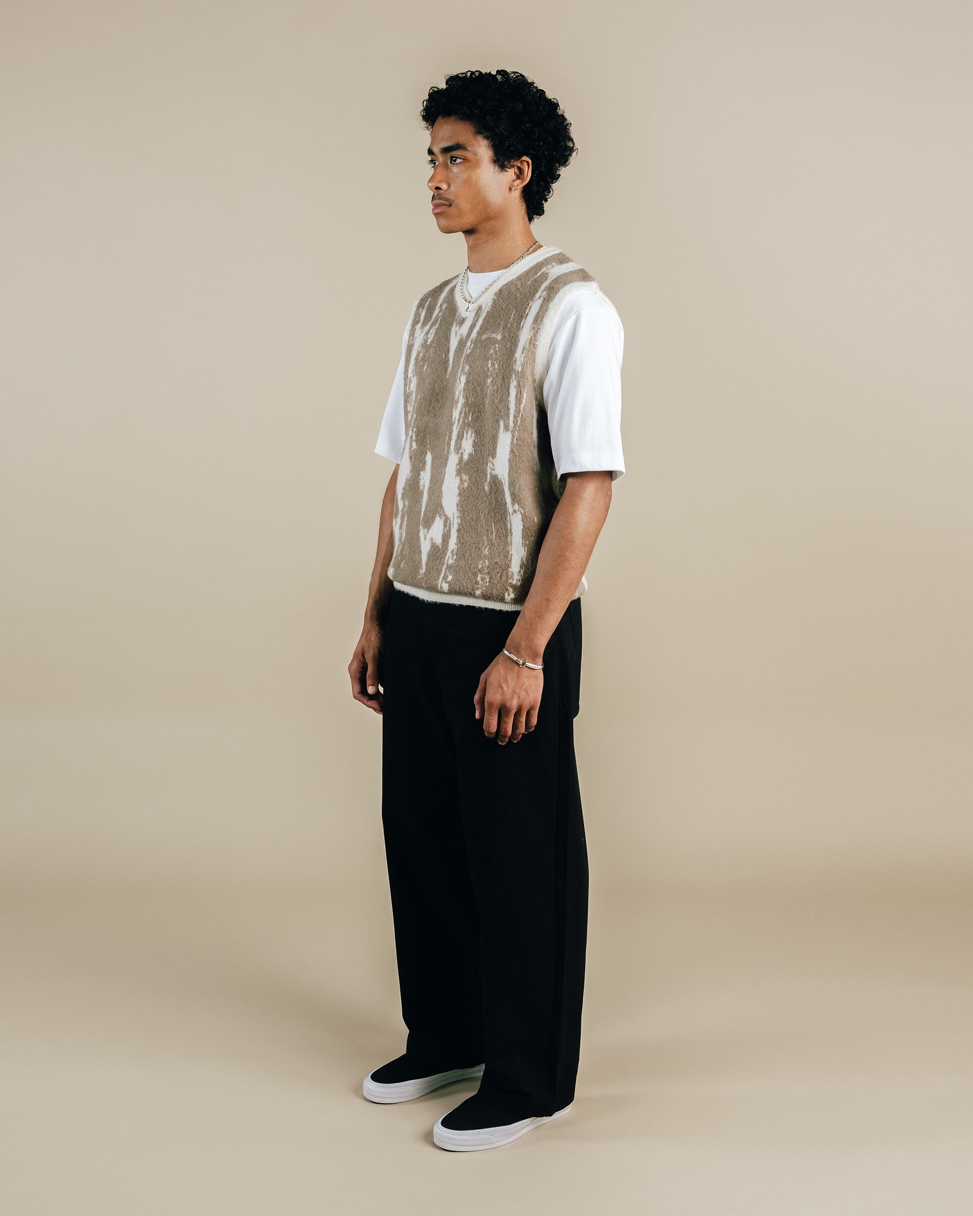 Man wearing a white shirt, beige vest, and black pants on a beige background