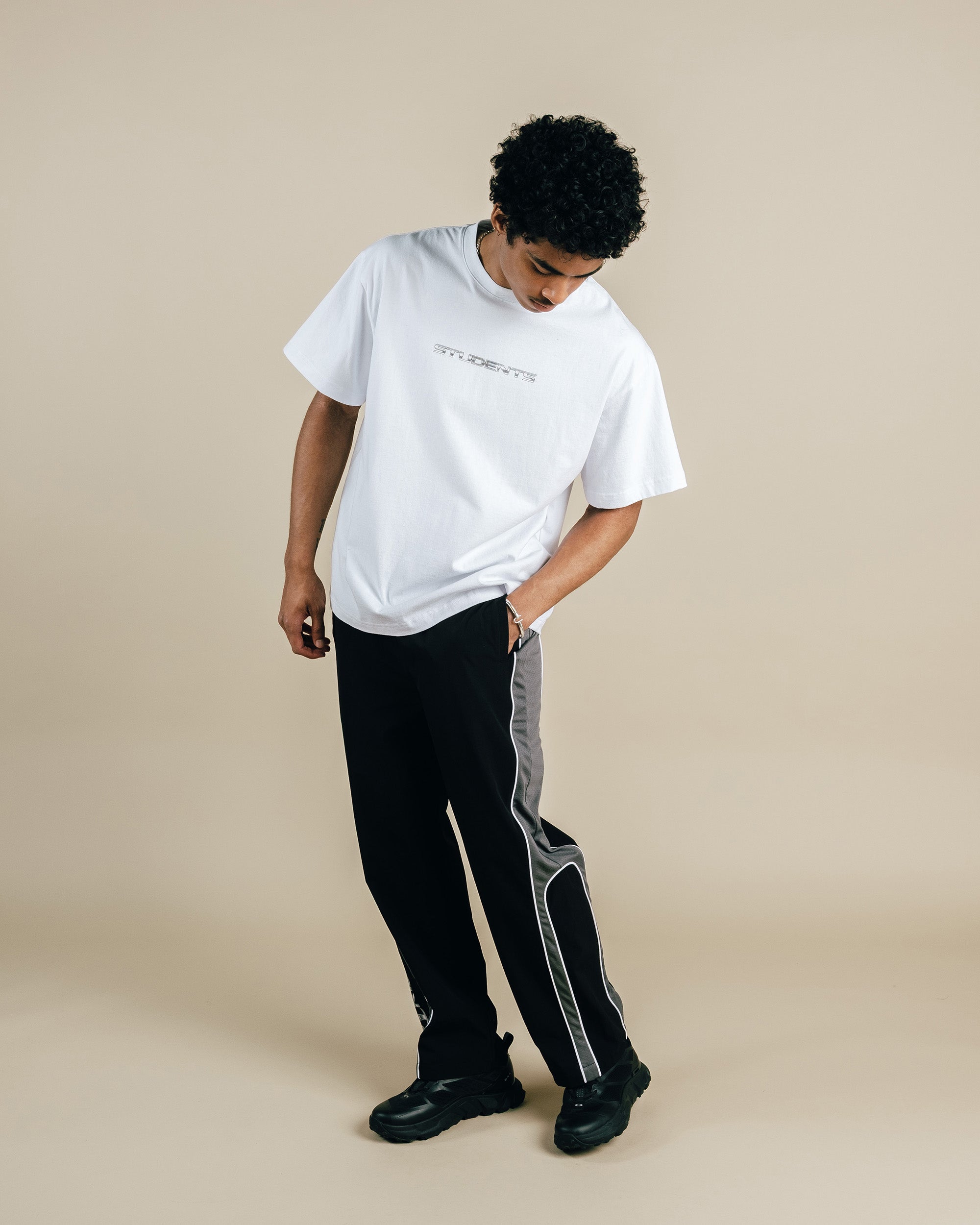 Person wearing a white t-shirt and black pants with gray stripes on a beige background