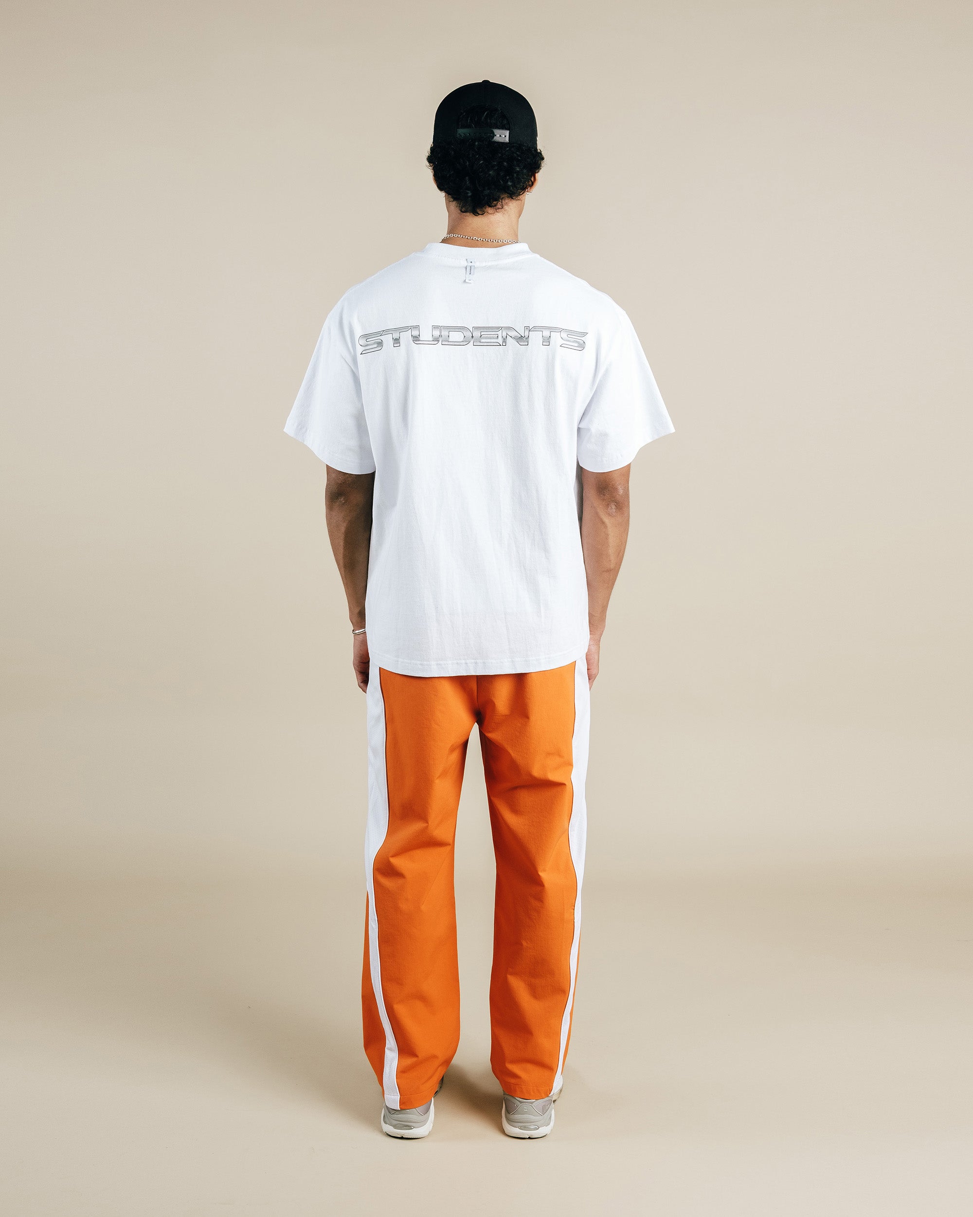 Person wearing a white t-shirt and orange pants on a beige background