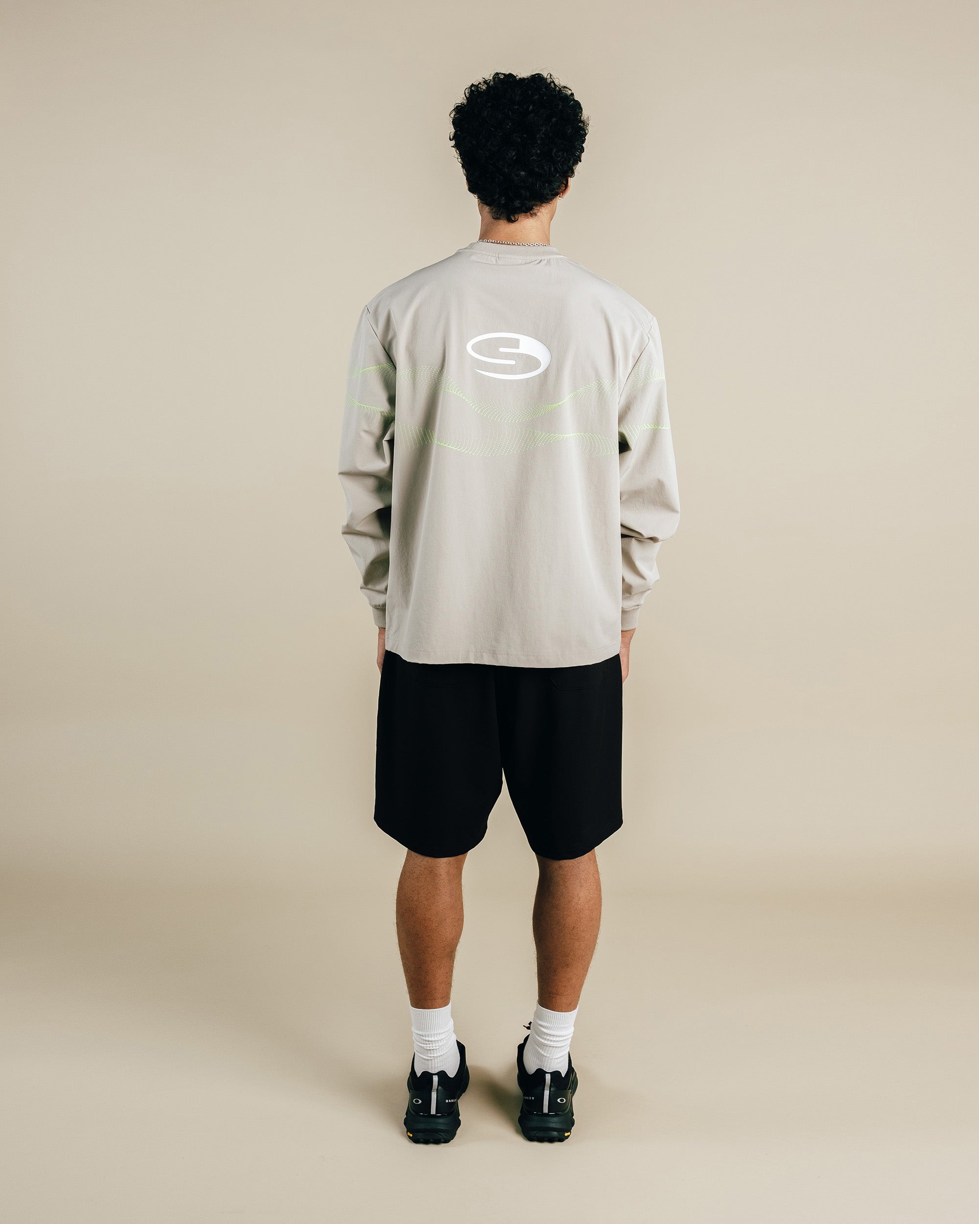 Person wearing a beige long-sleeve shirt with a logo on the back, standing against a beige background.