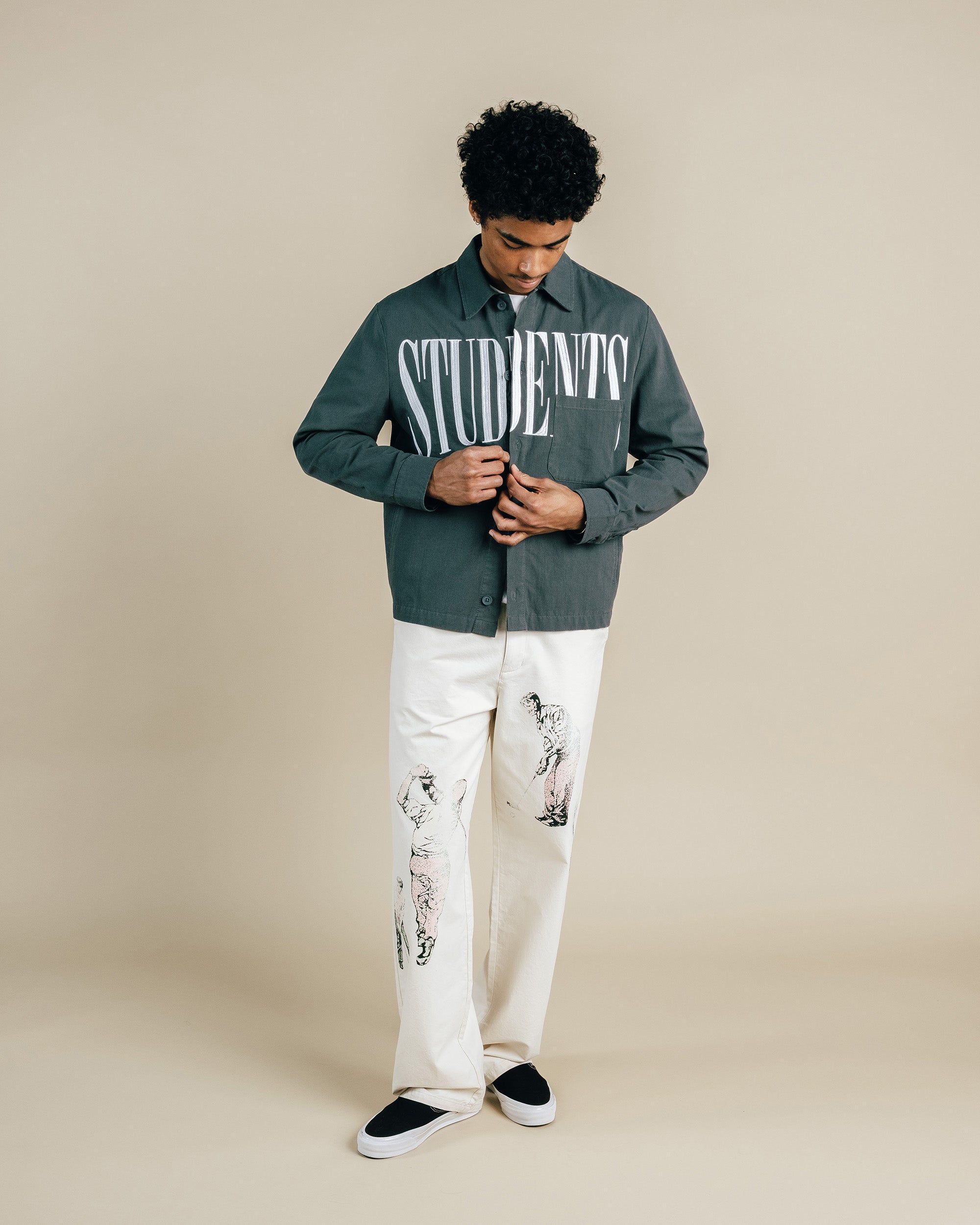 Person wearing a green shirt with 'STUDENT' text and white pants on a beige background