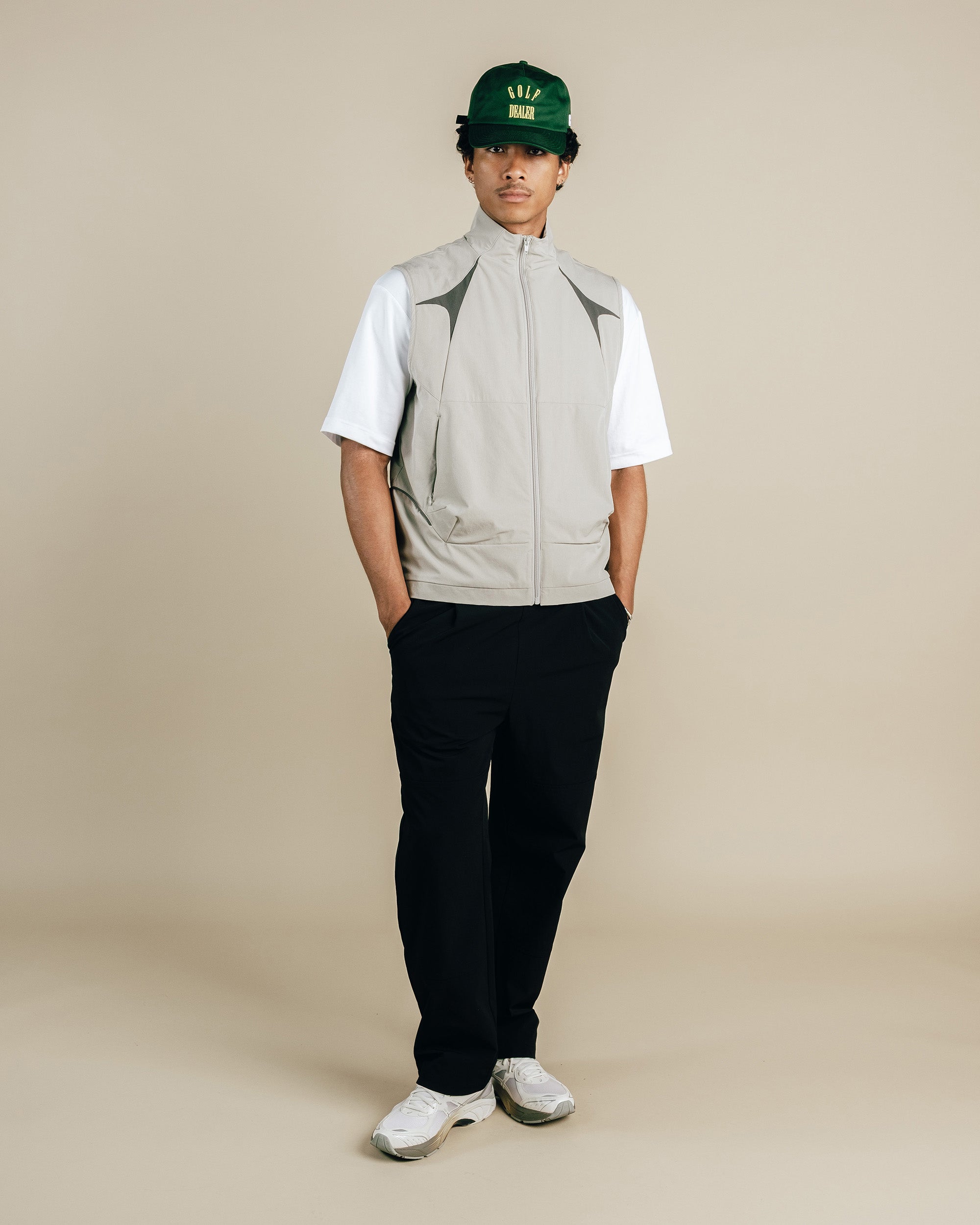 Person wearing a light gray vest over a white shirt with black pants on a beige background